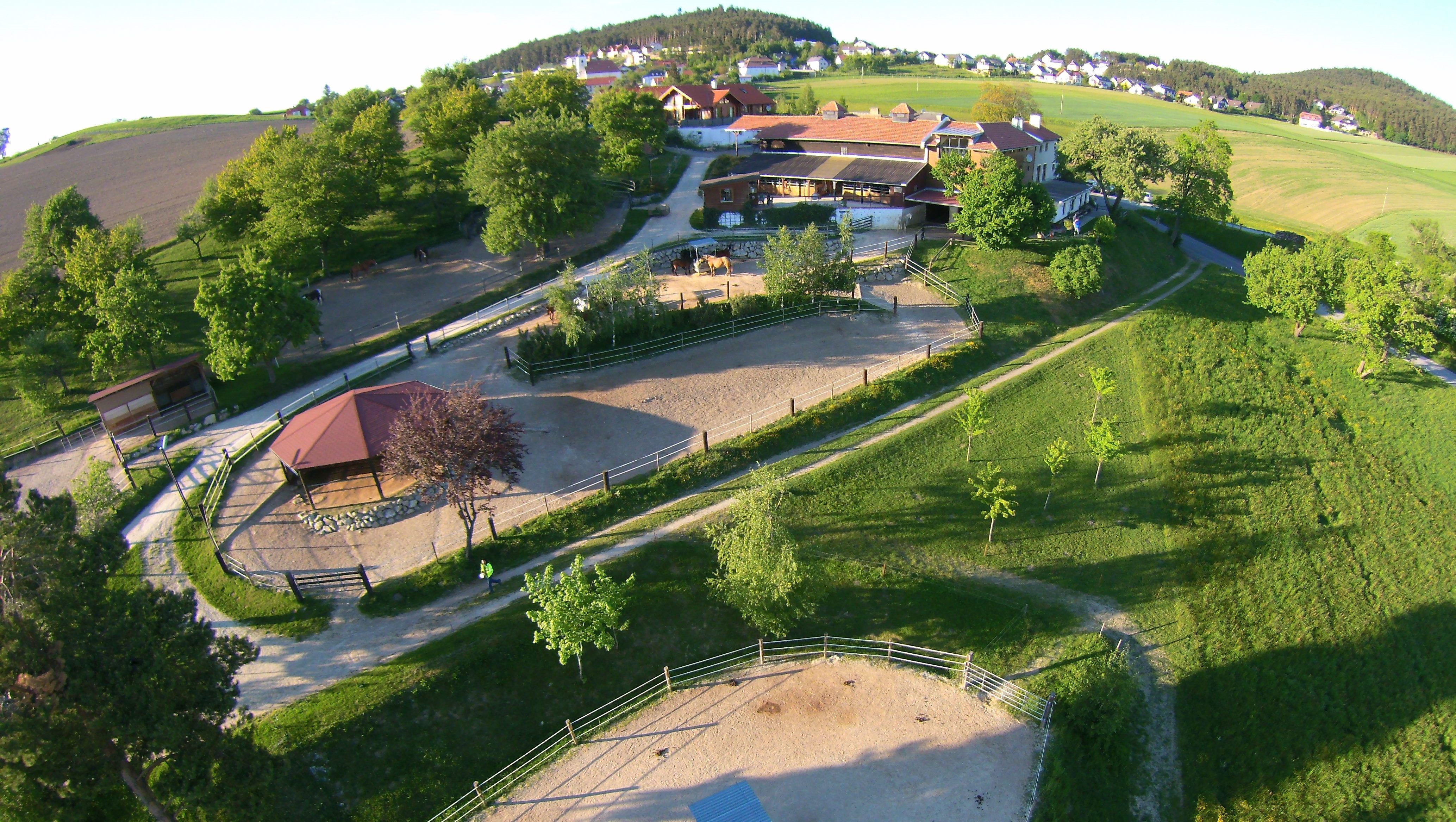 Luftaufnahme eines ländlichen Anwesens mit Gebäuden, Reitplätzen und grüner Landschaft.