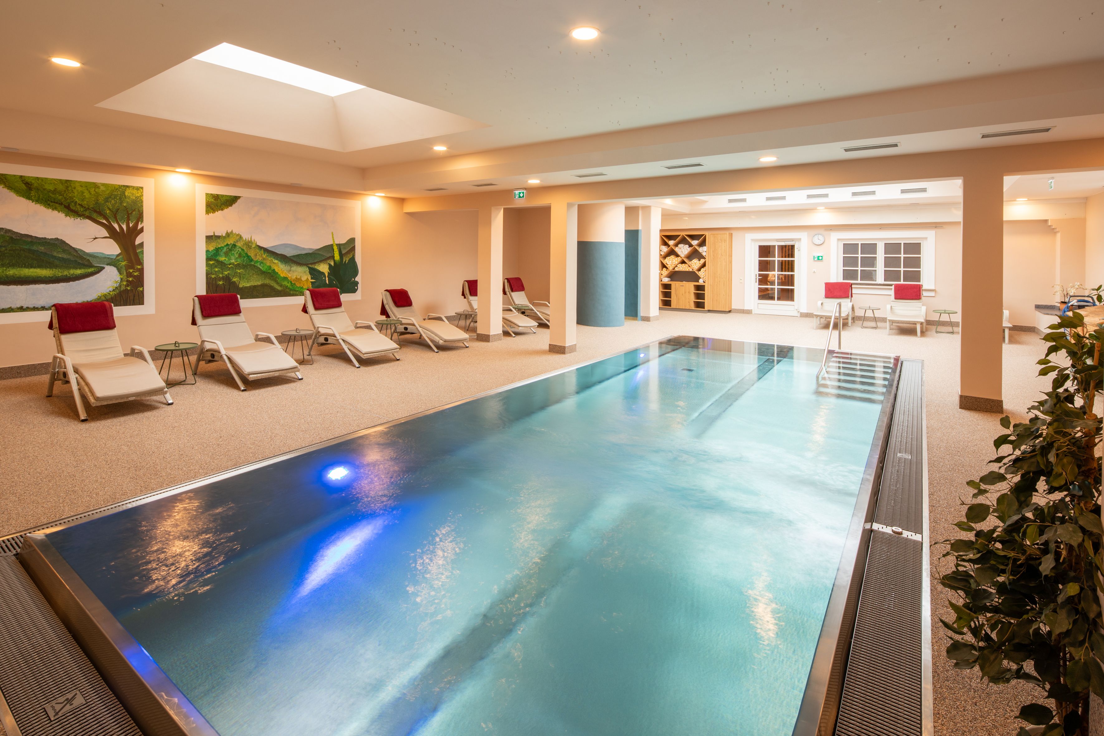Ein moderner Indoorpool im Hotel-Spa mit Liegestühlen und Wandmalereien