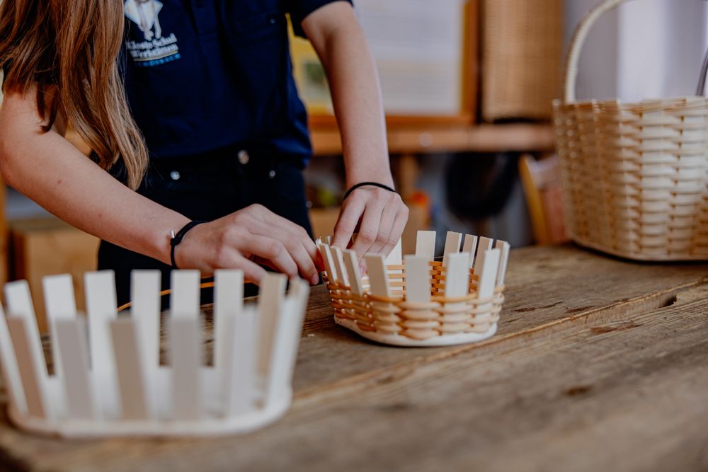 Person flechtet einen Korb auf einem Holztisch.
