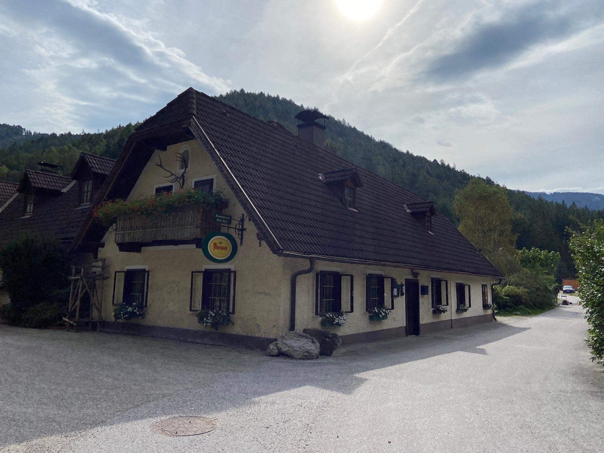 Traditionelles Gasthaus mit Blumenbalkon vor bewaldeten Hügeln.