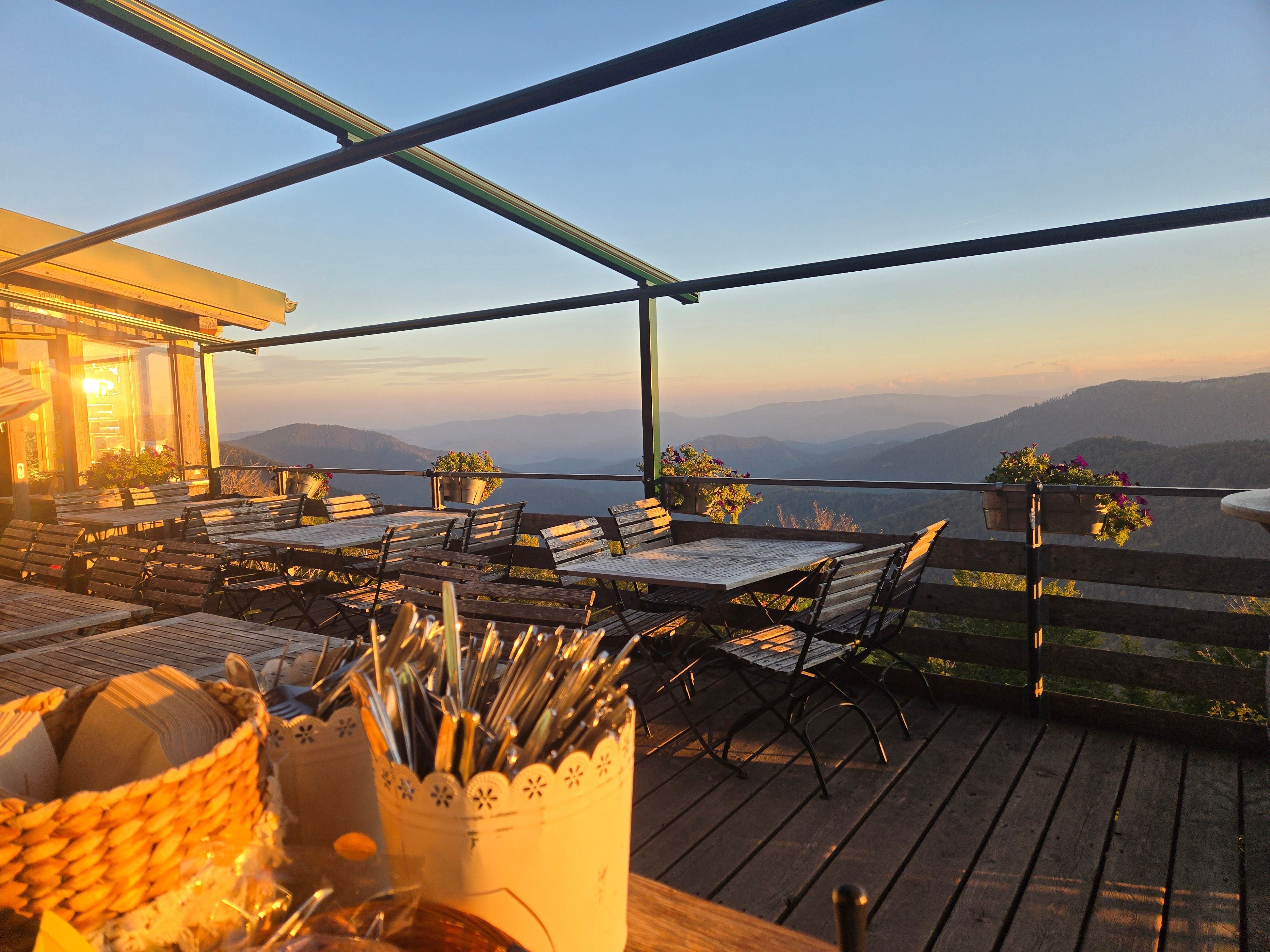 Terrasse der Enzianhütte mit Holztischen und Stühlen, Blick auf Berglandschaft im Abendlicht.