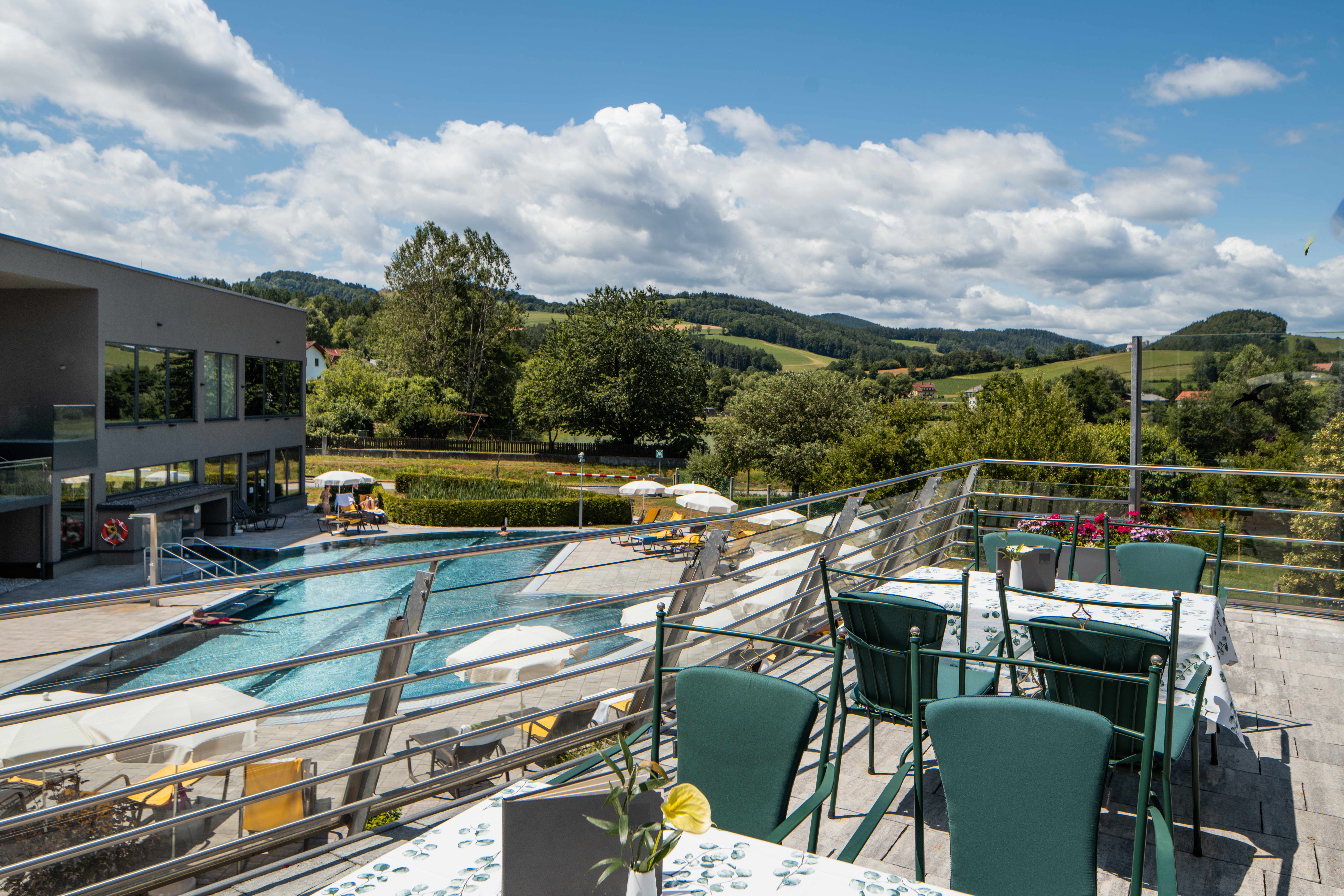 Terrasse mit Blick auf einen Pool und eine grüne Landschaft im Hintergrund.