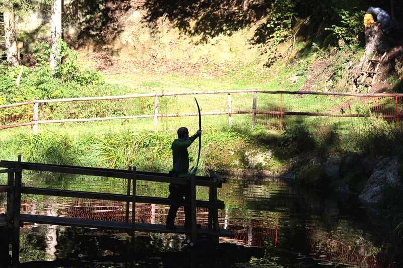 Person mit Bogen auf einer Brücke im Wald.