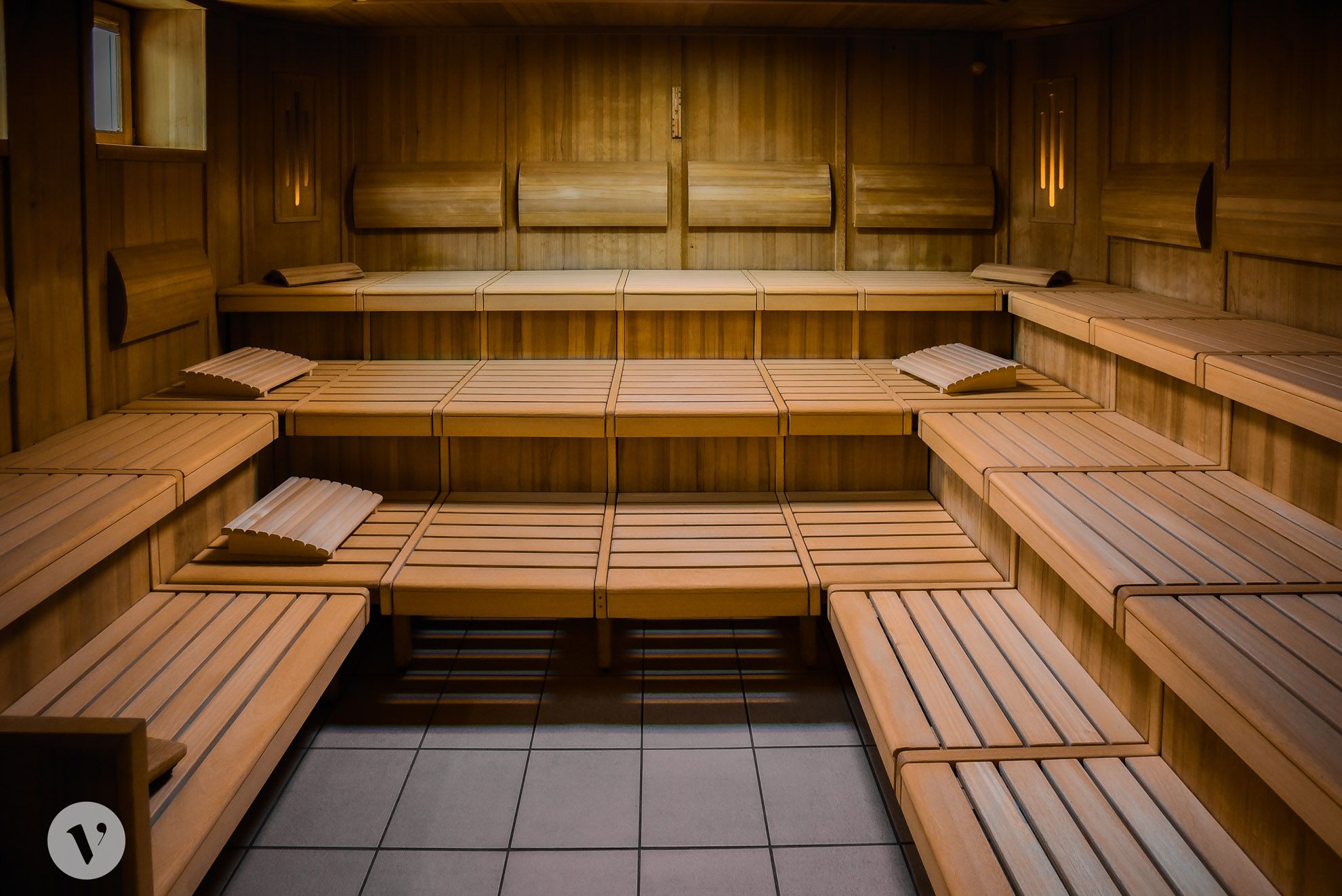 Innenansicht einer leeren Holzsauna mit mehreren Sitzreihen und Kopfstützen.