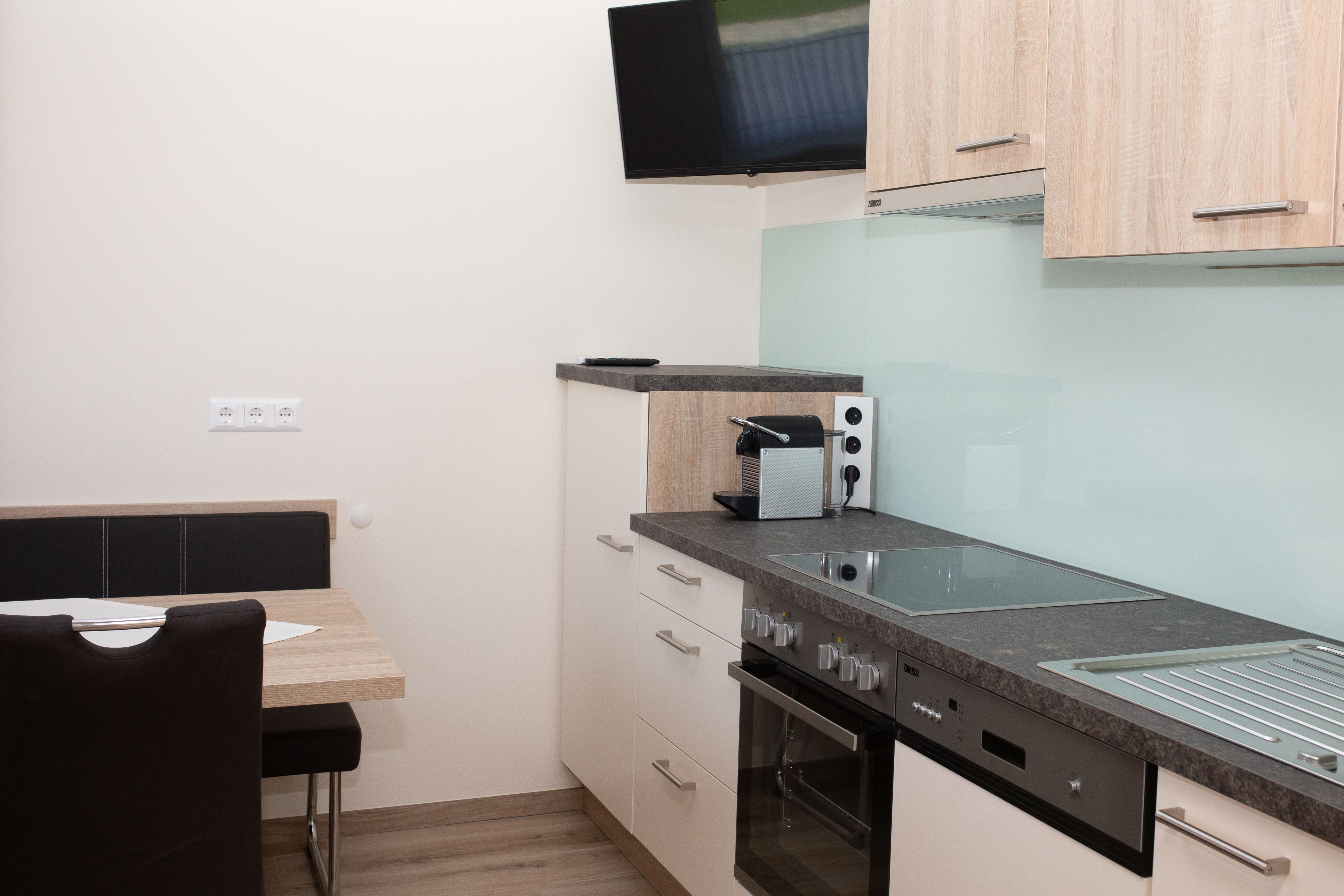 Moderne Küche mit Herd, Spüle, Kaffeemaschine und Wandfernseher.