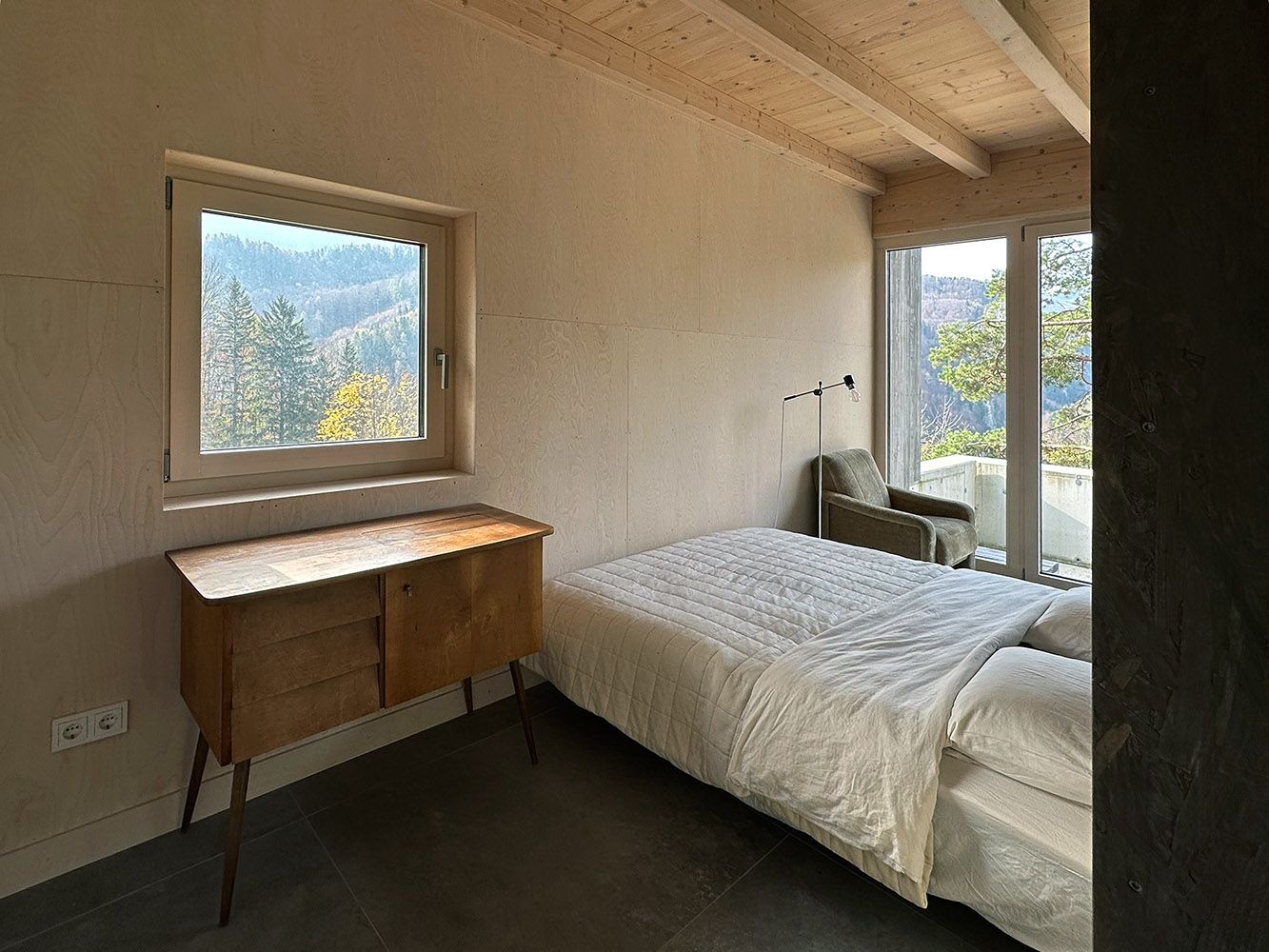 Schlafzimmer mit Bett, Holzdecke, Fenster mit Bergblick und Kommode.