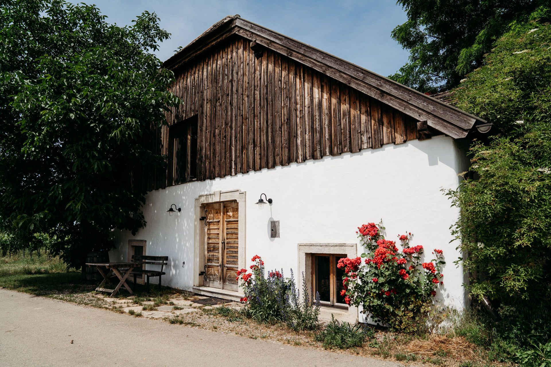 Außenansicht eines Hauses mit Holzwänden, weißen Wänden und roten Blumen im Vordergrund.