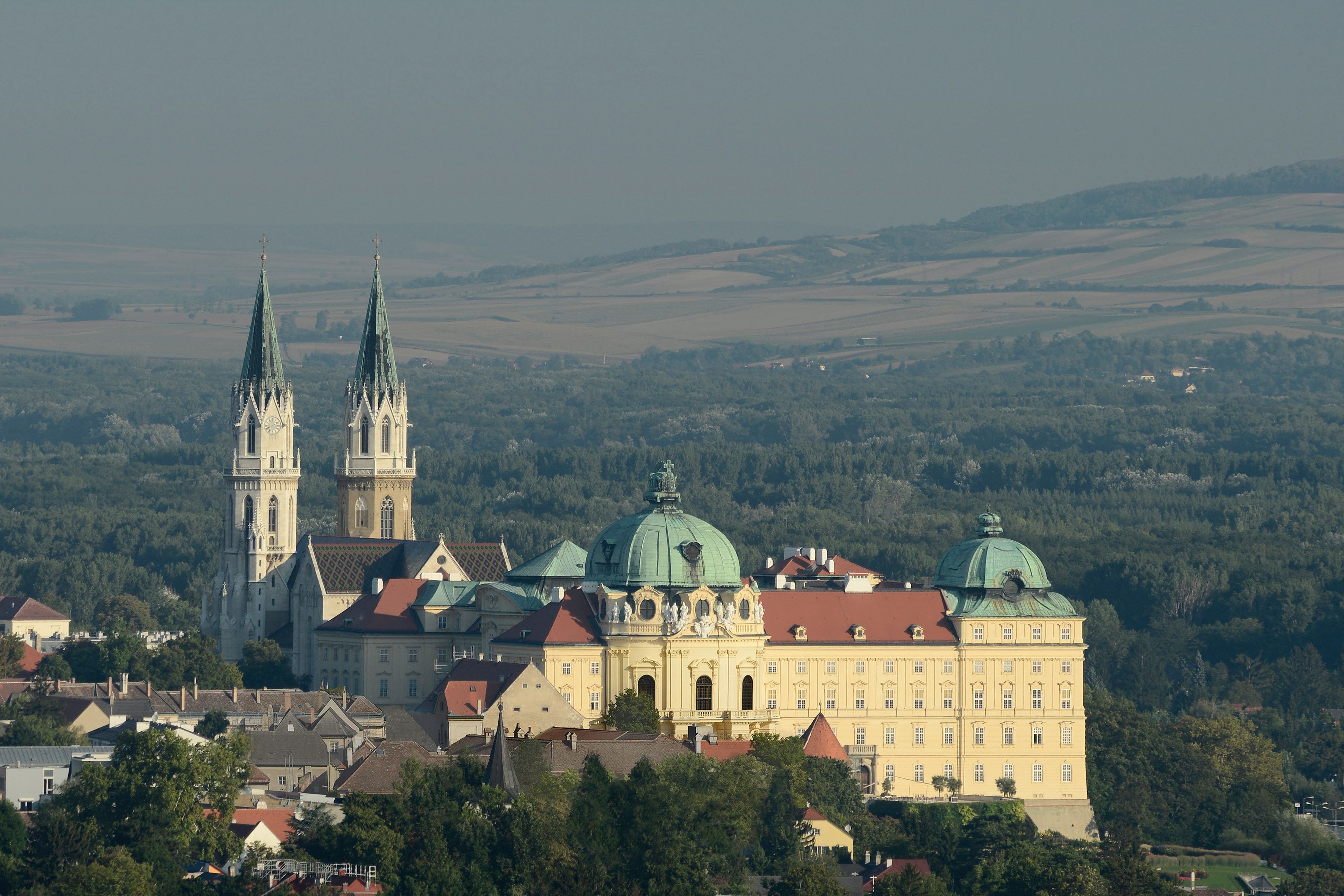 Luftaufnahme des Stifts Klosterneuburg mit zwei Kirchtürmen und umliegender Landschaft.