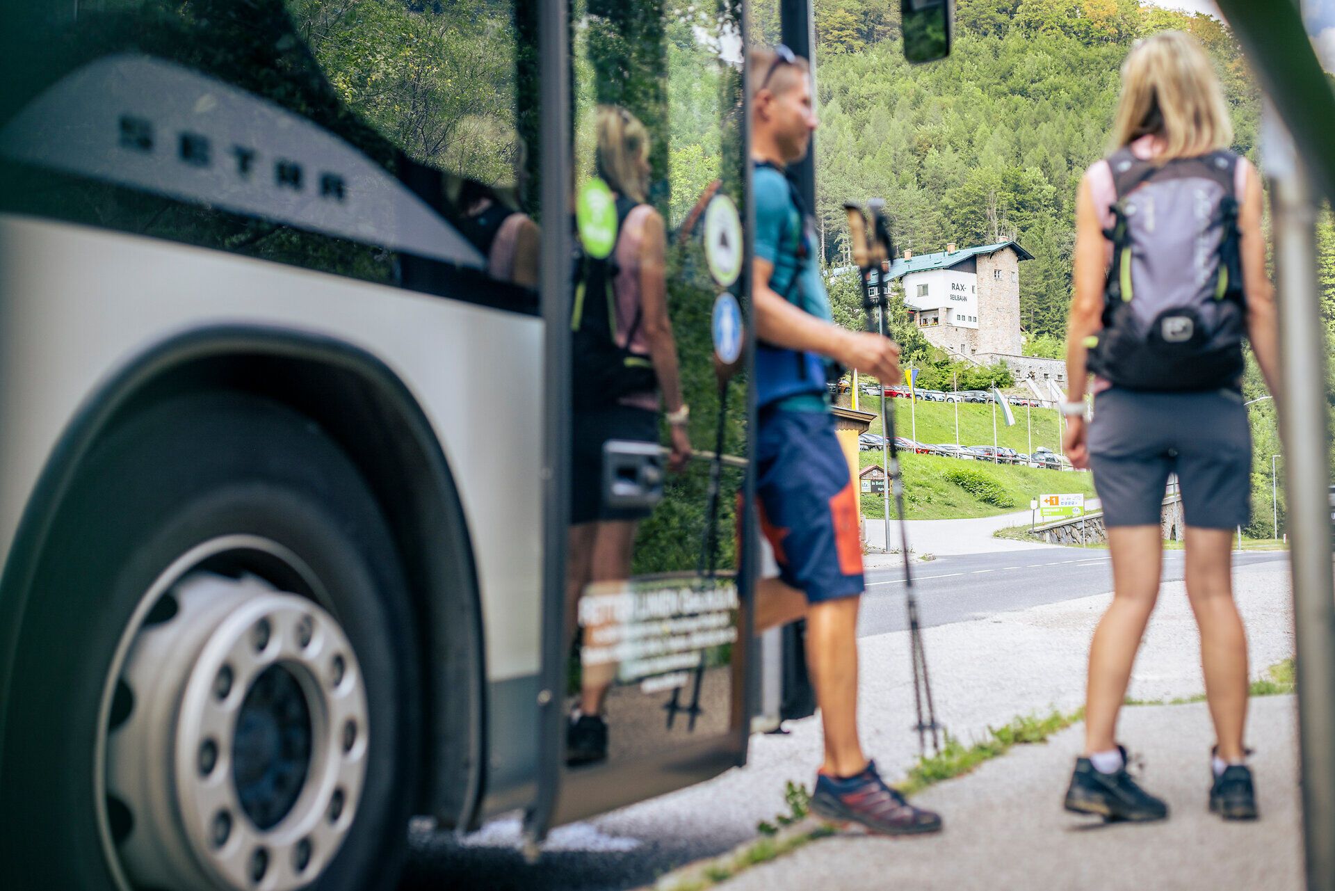 Wandernde steigen mit Rucksäcken an einer Haltestelle aus einem Bus aus.