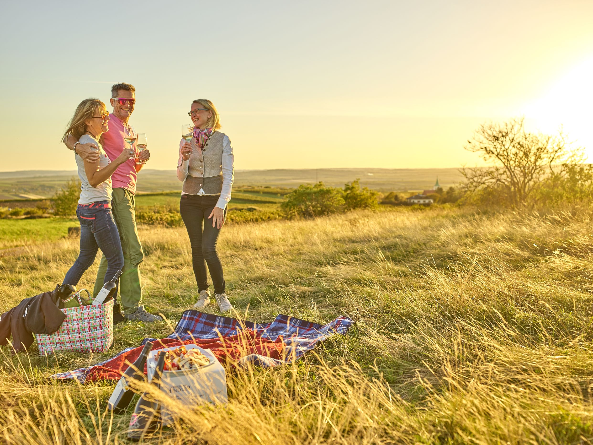 Drei Personen beim Picknick auf einer Wiese bei Sonnenuntergang.