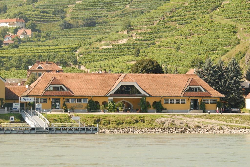 Gelbes Gebäude mit rotem Dach vor Weinbergen in Spitz an der Donau.