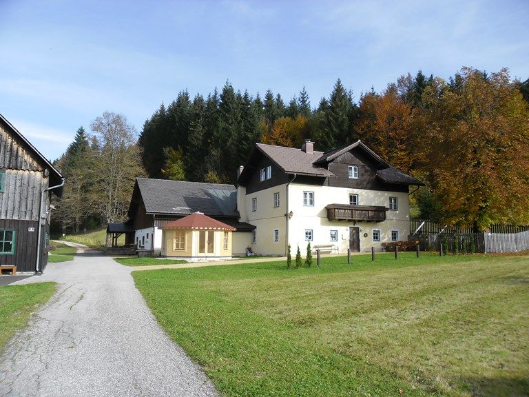 Ein großes, zweistöckiges Haus mit Balkon, umgeben von Wiesen und Bäumen im Herbst.