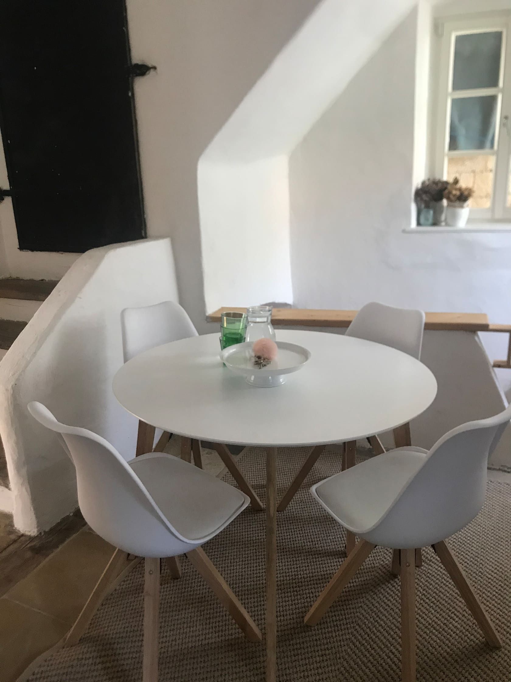 Moderne Sitzecke mit rundem Tisch und vier weißen Stühlen in einem hellen Raum.