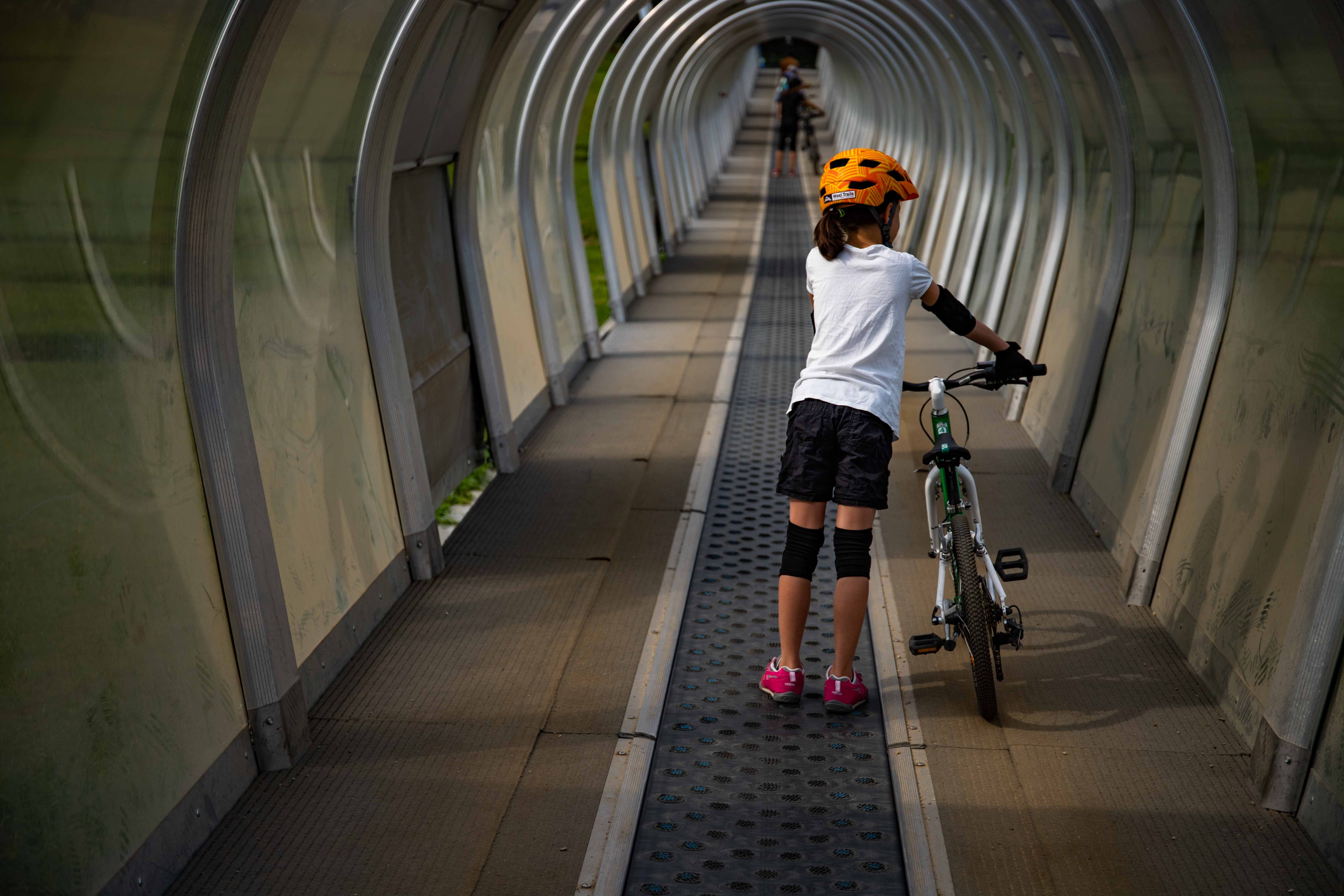 Kind mit Fahrrad auf Förderband im überdachten Tunnel.