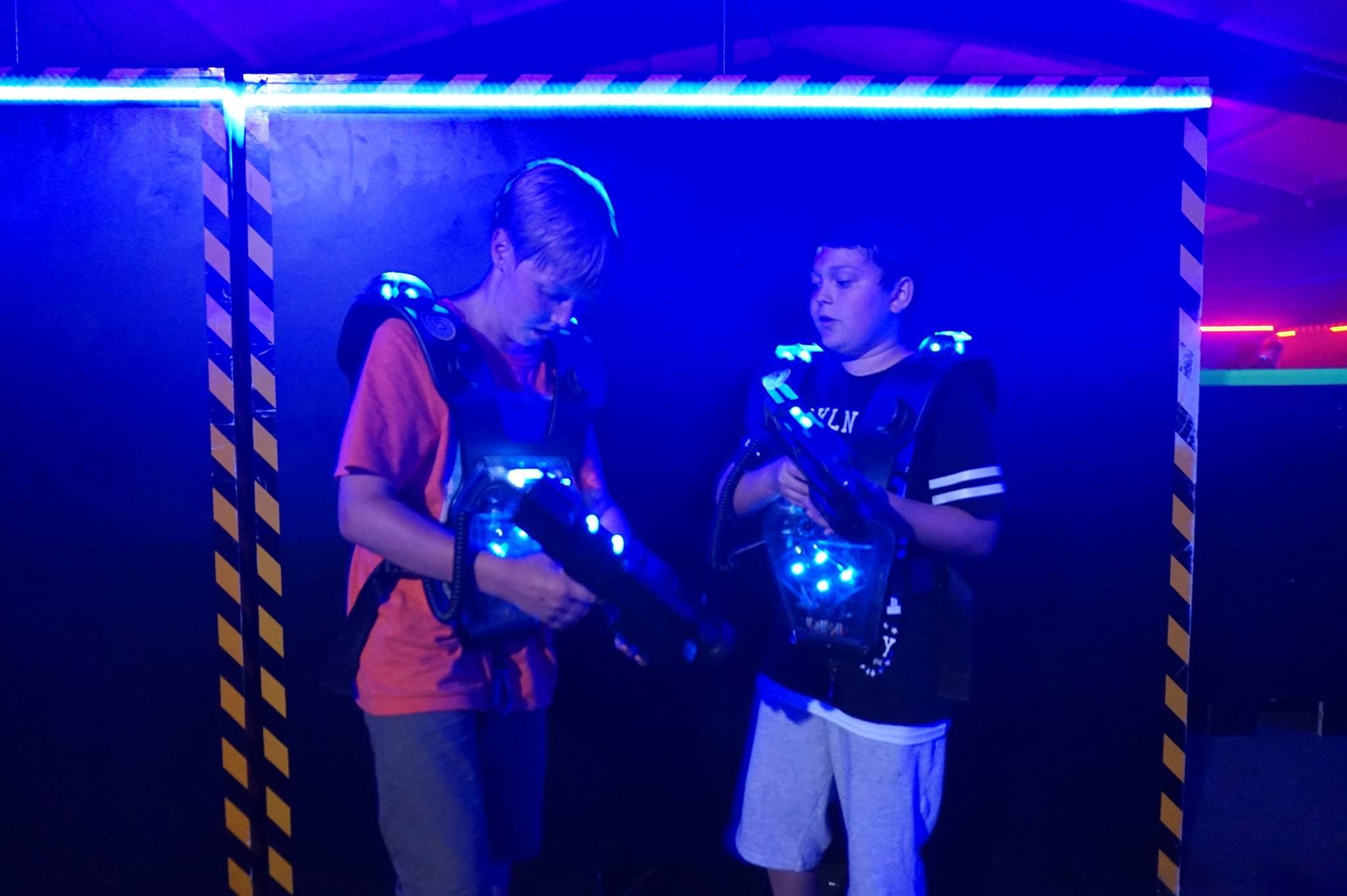 Zwei Jungen in einer Laser-Tag-Arena mit leuchtenden Westen und Laserpistolen.