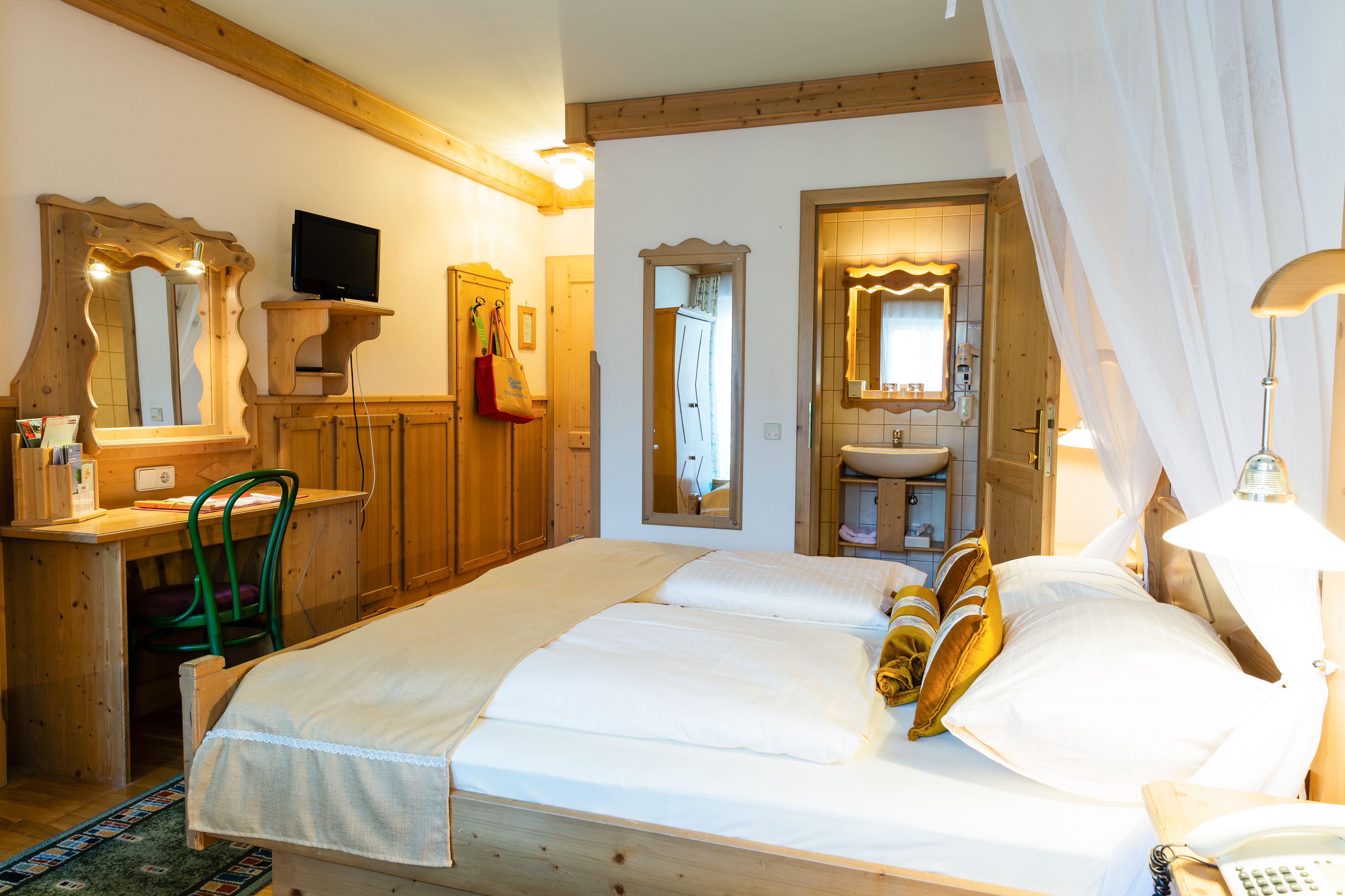 Gemütliches Hotelzimmer mit Doppelbett, Holzmöbeln und kleinem Badezimmer.