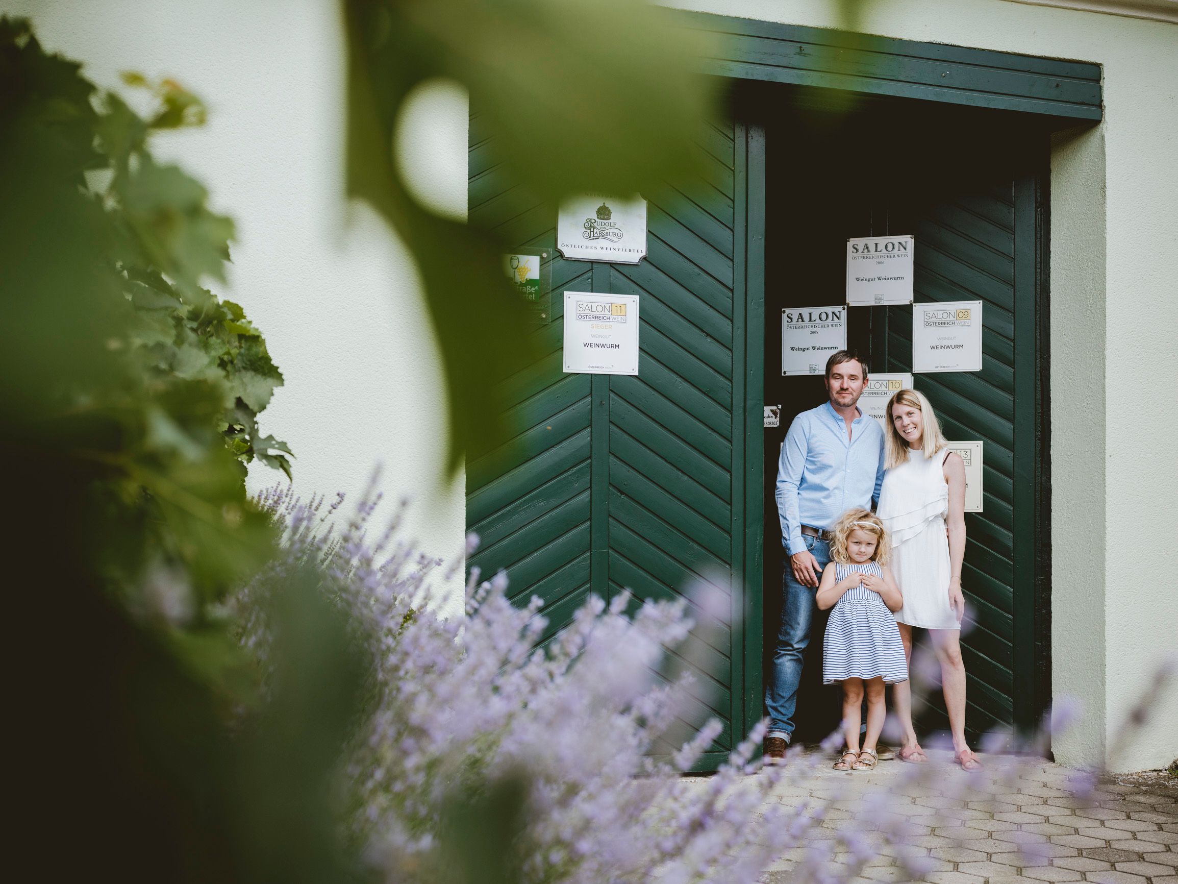 Eine Familie steht vor einem grünen Tor, umgeben von Lavendel und Pflanzen.