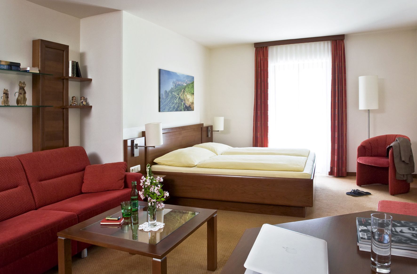 Gemütliches Hotelzimmer mit Doppelbett, rotem Sofa, Glastisch und Dekorationen.