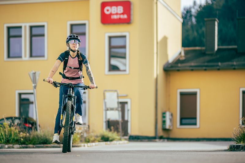 Person auf Fahrrad vor gelbem Gebäude mit ÖBB-Logo.