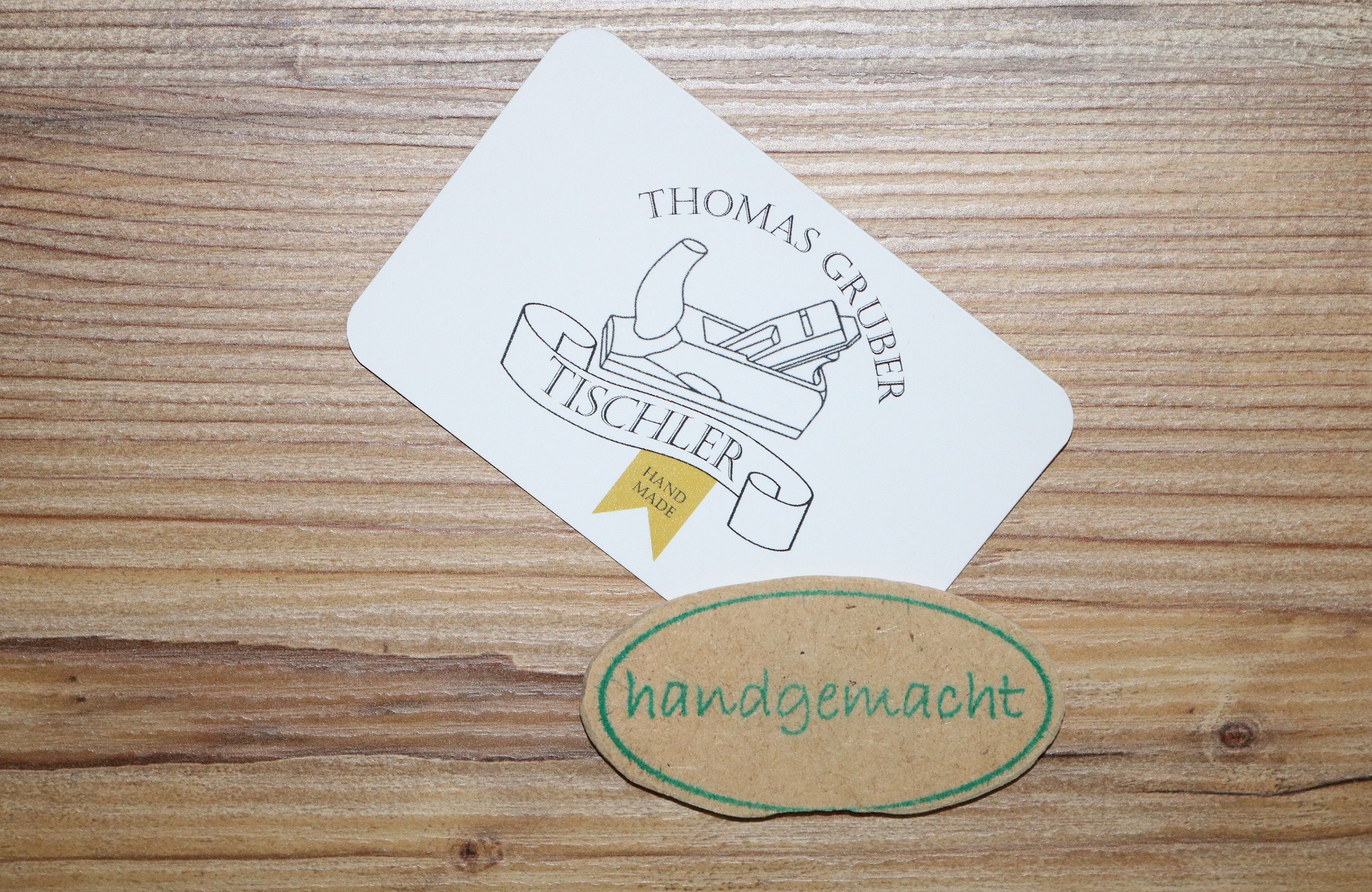 Visitenkarte von Tischler Thomas Gruber mit einem Hobel-Logo und einem handgemachten Etikett auf Holzuntergrund.