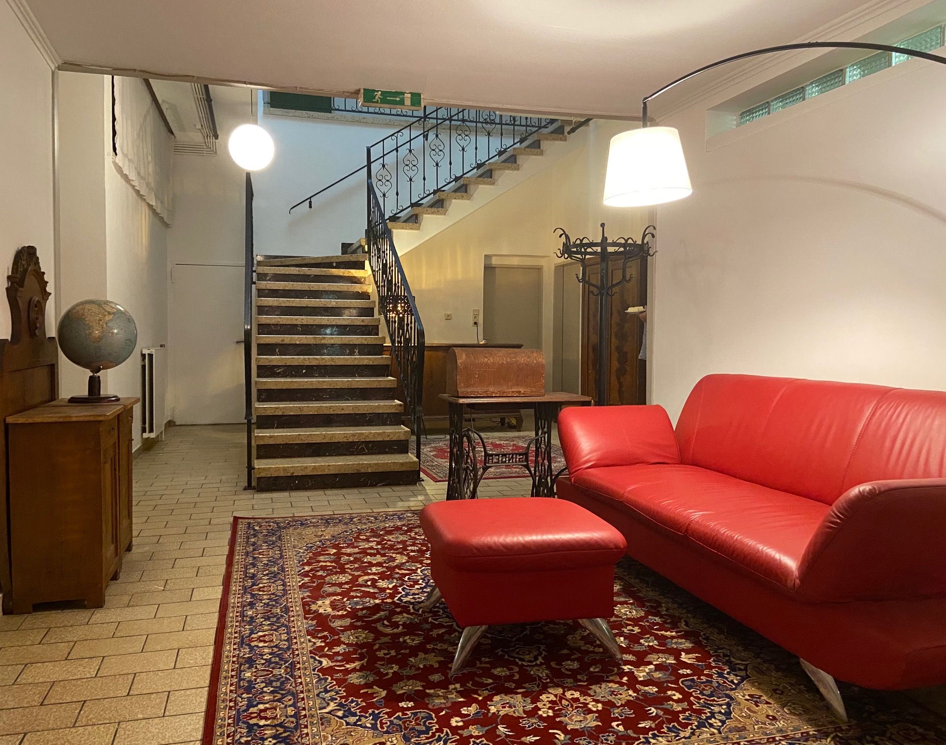 Ein Foyer mit rotem Sofa, Teppich, Globus und Treppe.