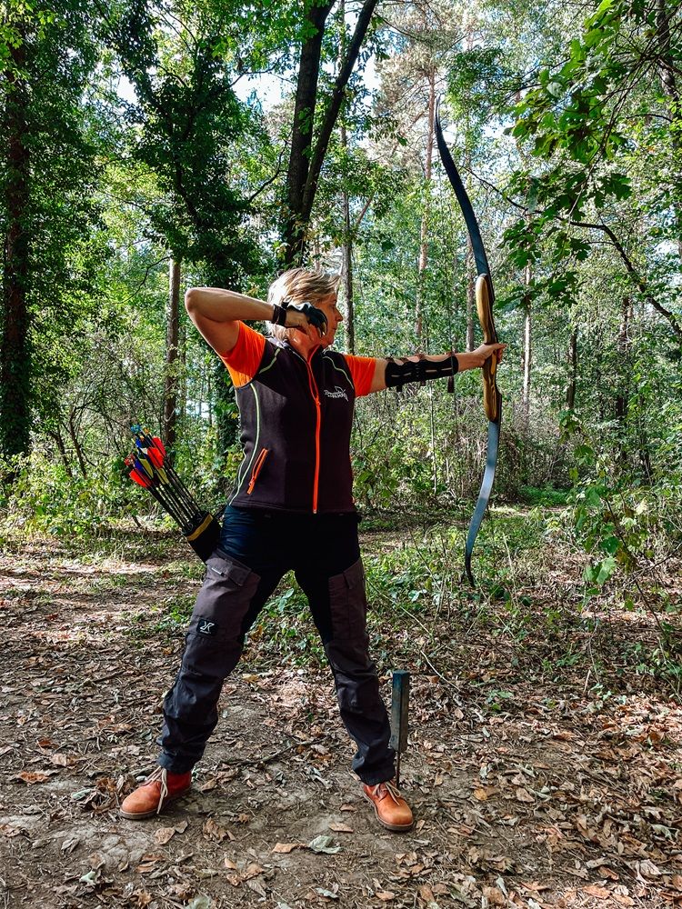 Person beim Bogenschießen im Wald mit Pfeil und Bogen.