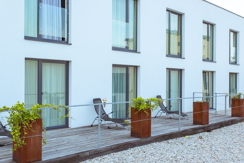 Moderne Terrasse mit Liegestühlen und Pflanzen vor einem Gebäude mit großen Fenstern.