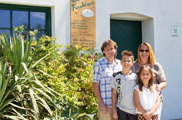 Eine Familie steht vor einem Gebäude mit einem Schild des Weinguts Fürnkranz.