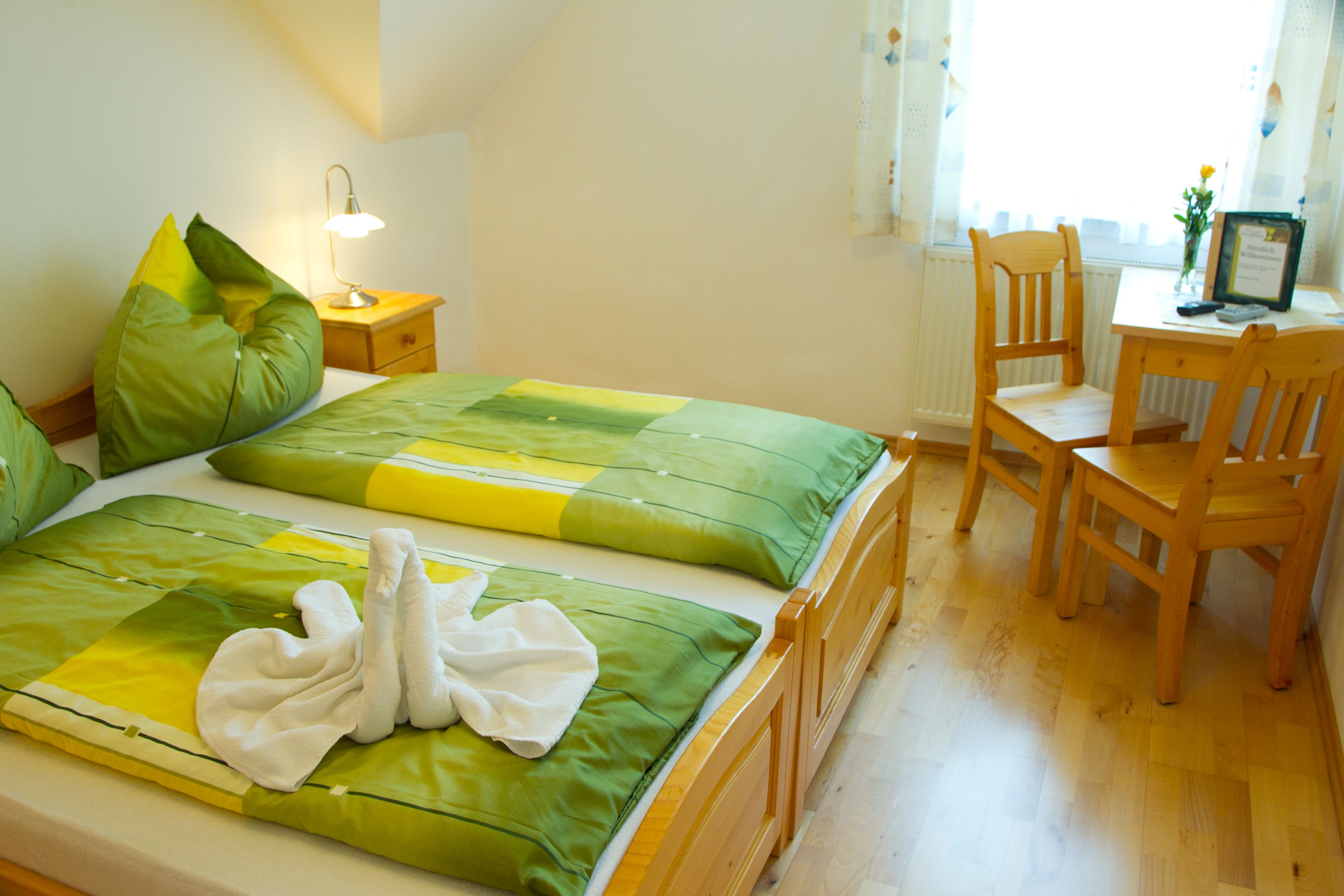 Gemütliches Gästezimmer mit Doppelbett, grüner Bettwäsche und Holzmöbeln.