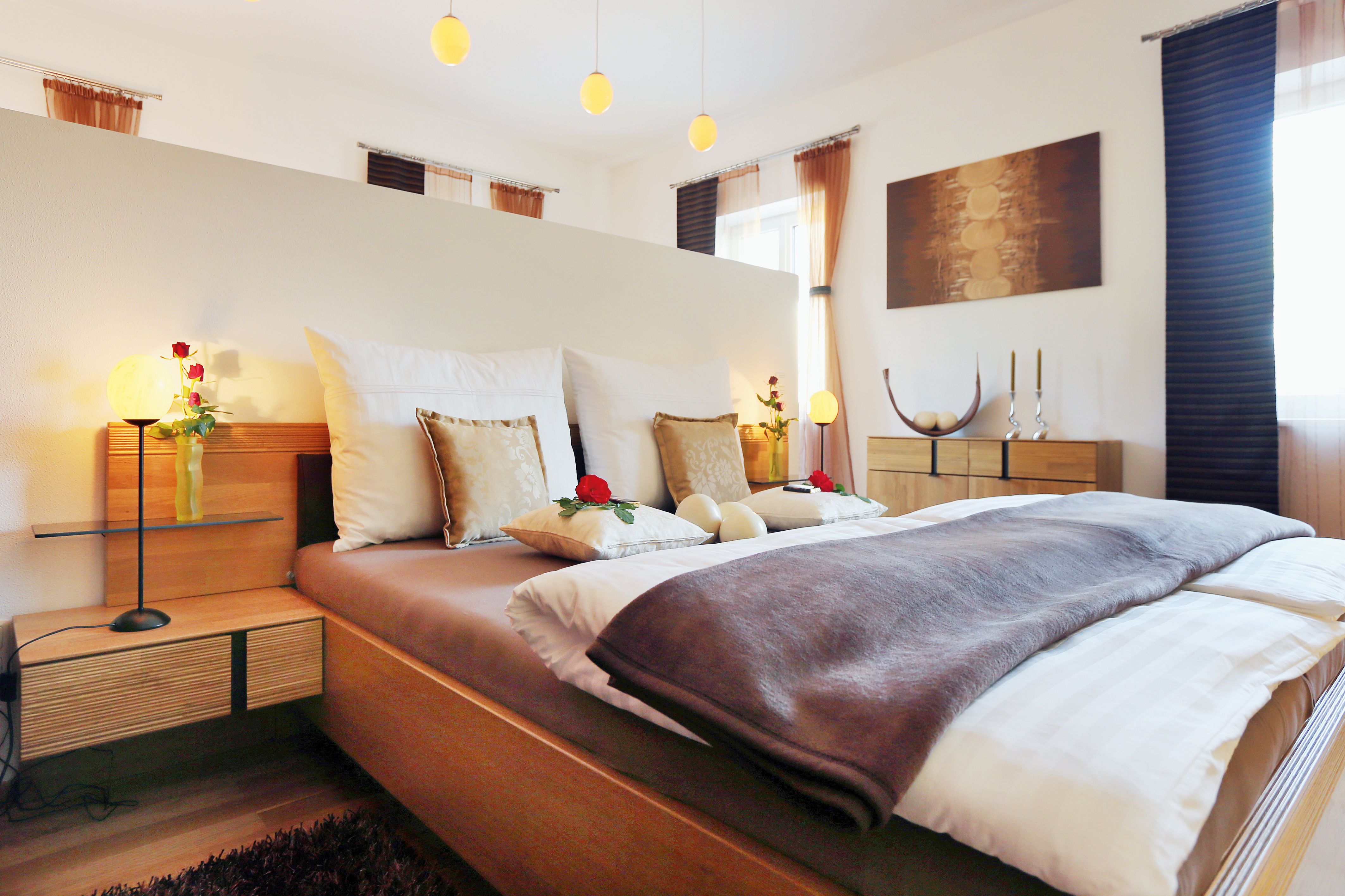 Gemütliches Schlafzimmer mit Doppelbett, dekoriert mit Kissen und Rosen, Holzmöbeln und sanfter Beleuchtung.