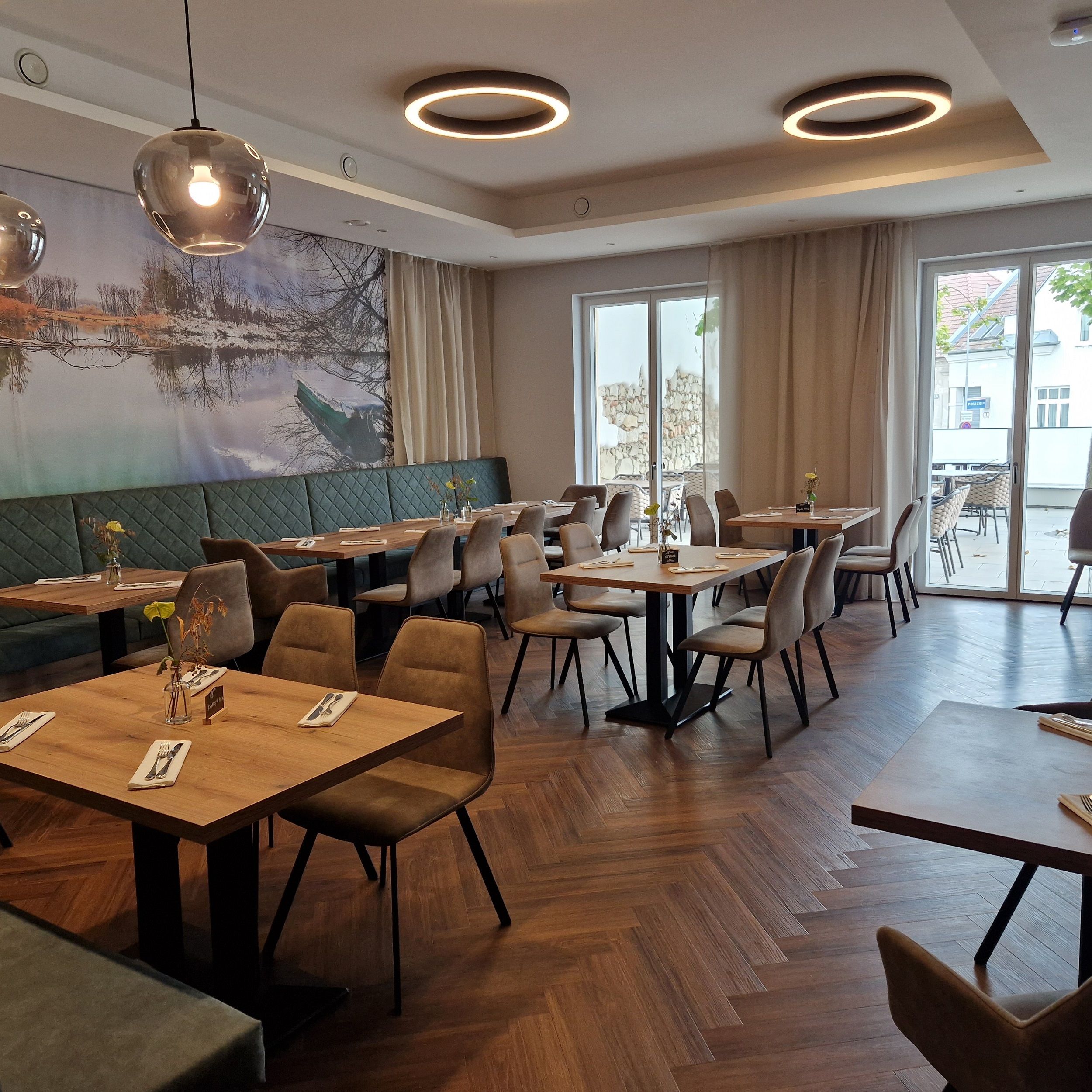 Innenansicht eines modernen Restaurants mit Holzboden, Tischen und Stühlen.