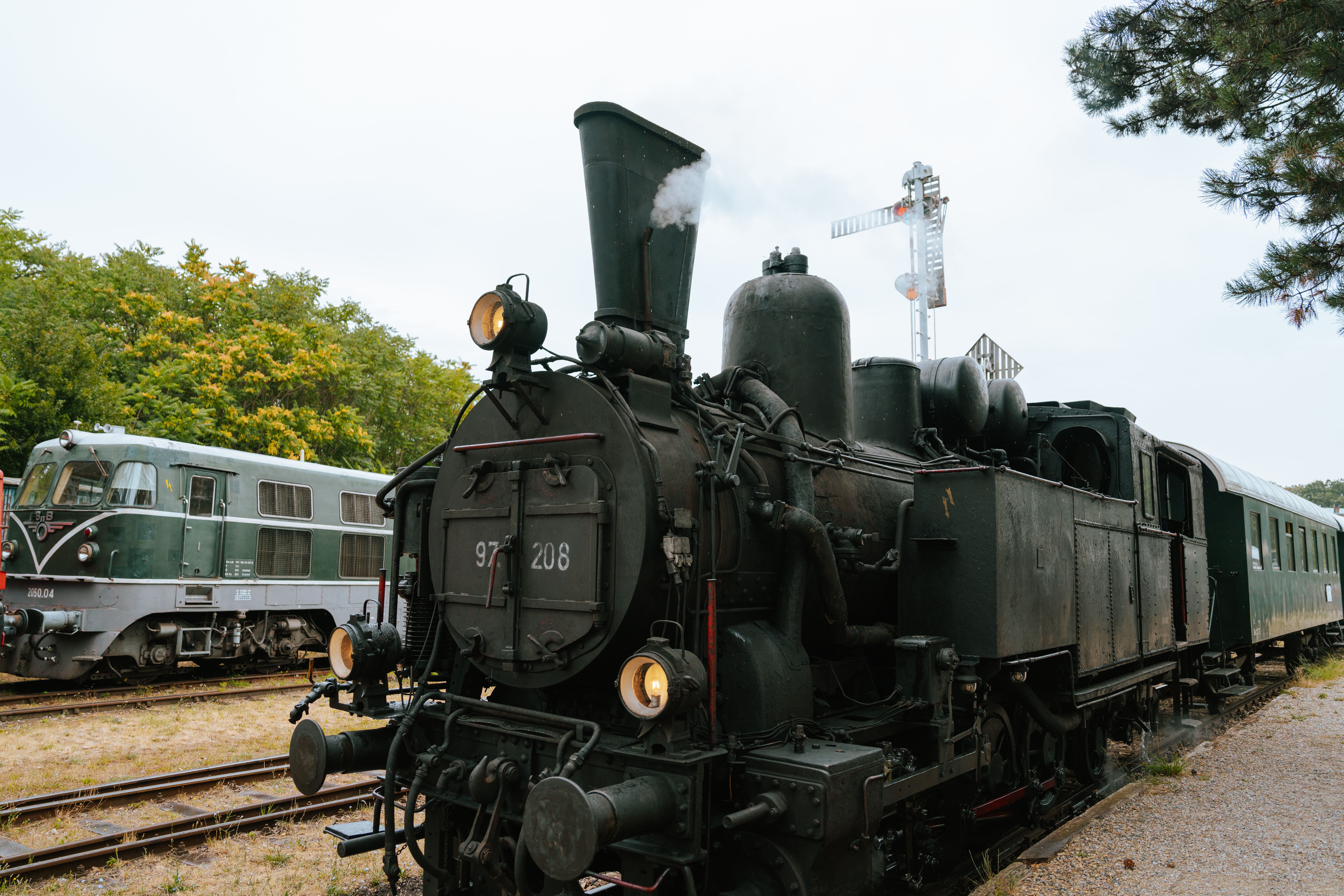Im Eisenbahnmuseum Strasshof erwacht die Geschichte der Dampflokomotiven zum Leben. Die majestätische Lokomotive dampft sanft vor sich hin und versetzt die Besucher in eine vergangene Zeit, während die umgebenden Bäume eine ruhige Kulisse bieten. Hier können Eisenbahnfans und Neugierige die Faszination der alten Bahntechnik hautnah erleben.