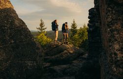 Zwei Wanderer stehen zwischen imposanten Felsformationen und genießen den weiten Blick auf die Waldlandschaft im goldenen Morgenlicht im Waldviertel.