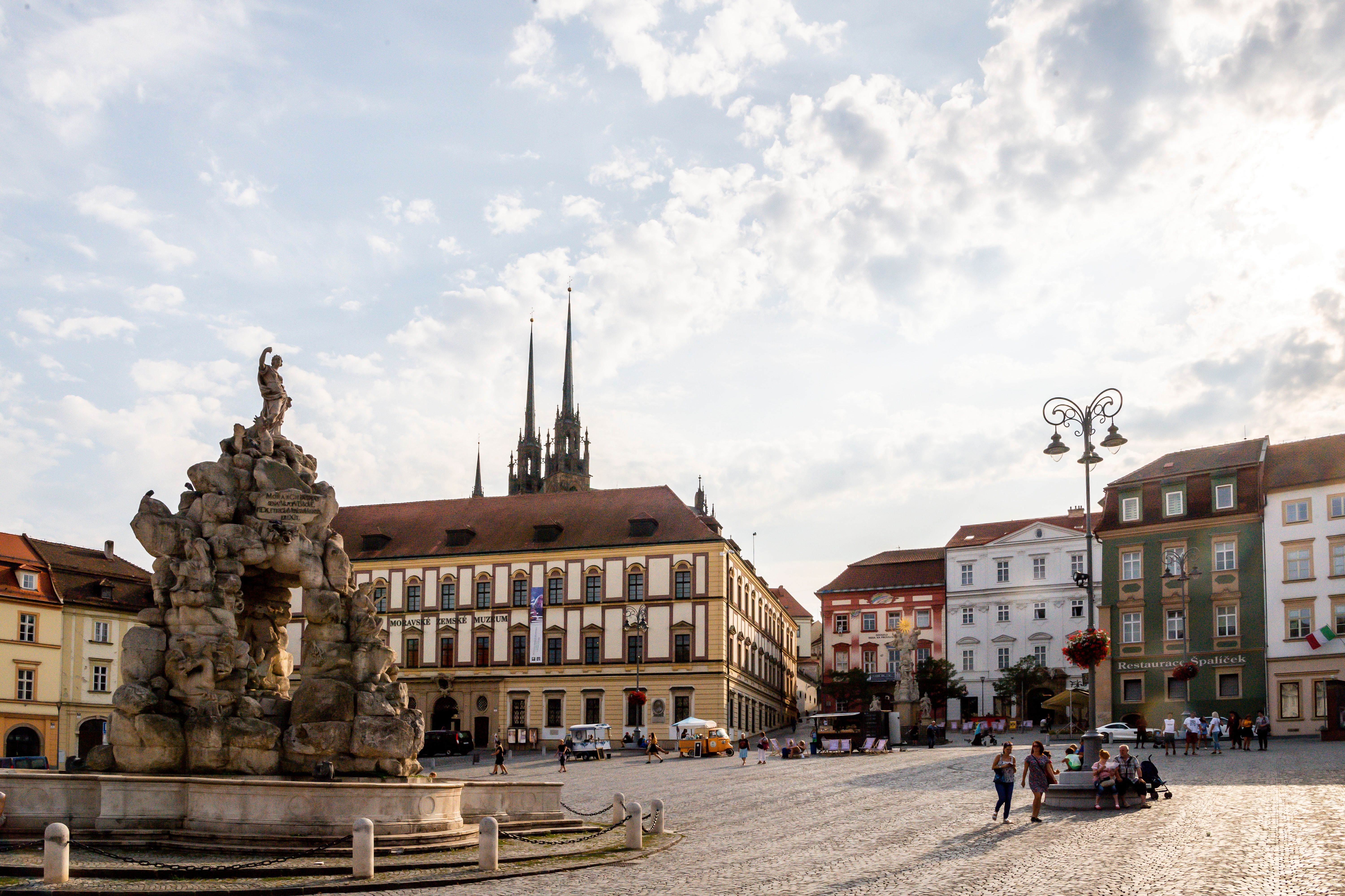 Ein Platz in Brünn mit einem Brunnen im Vordergrund und einer Kirche im Hintergrund.