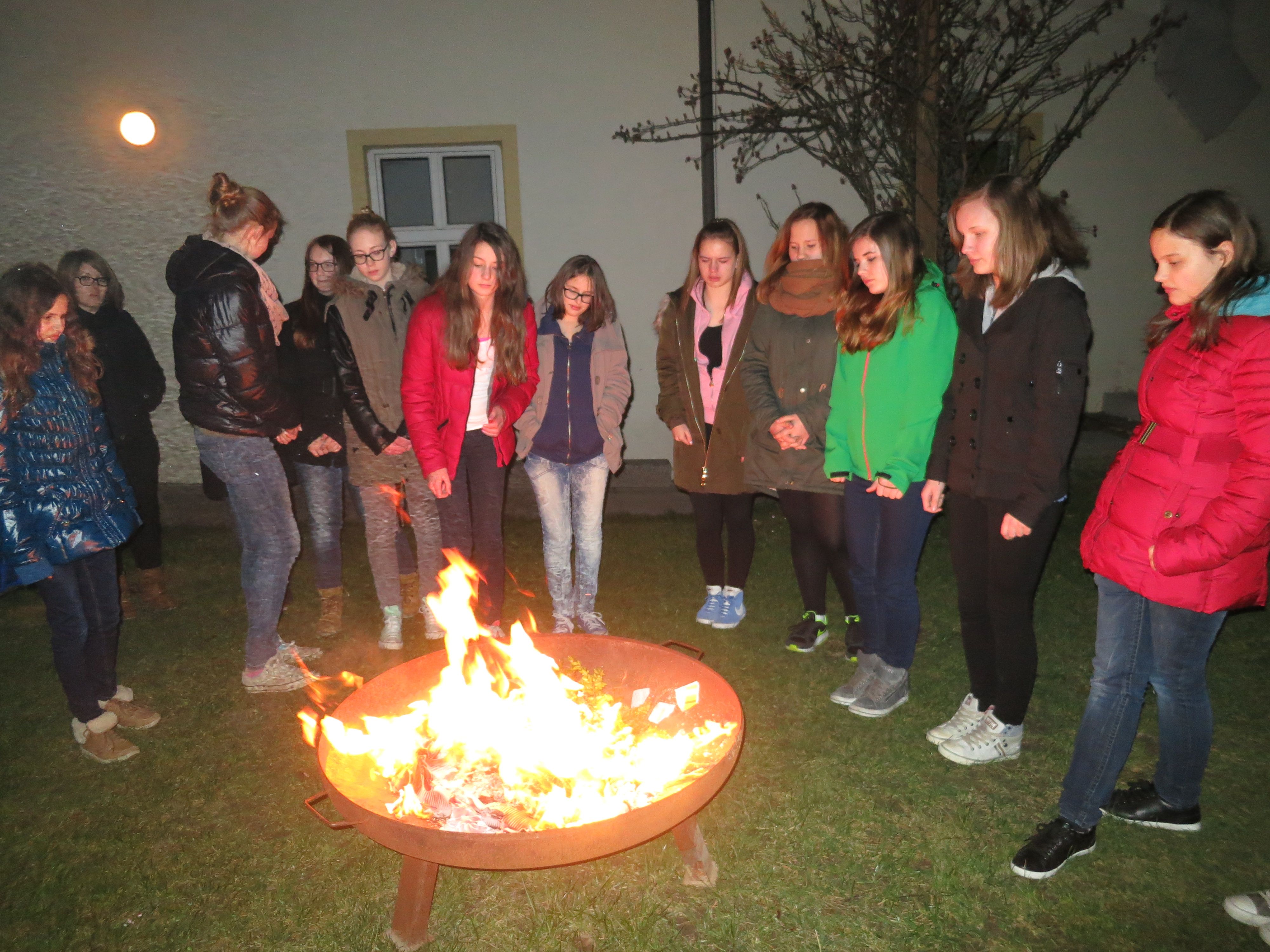 Gruppe von Jugendlichen steht um eine Feuerstelle im Freien.