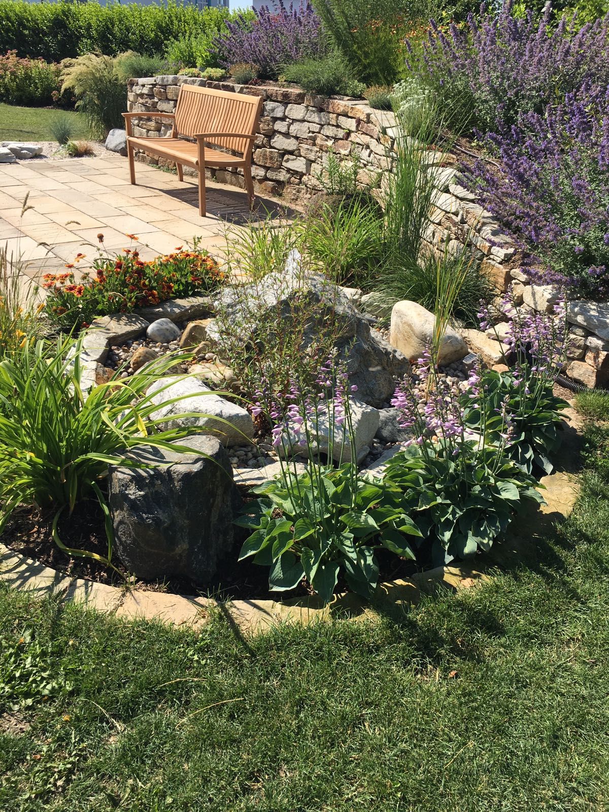 Garten mit Steinmauer, Bank und Blumenbeet.