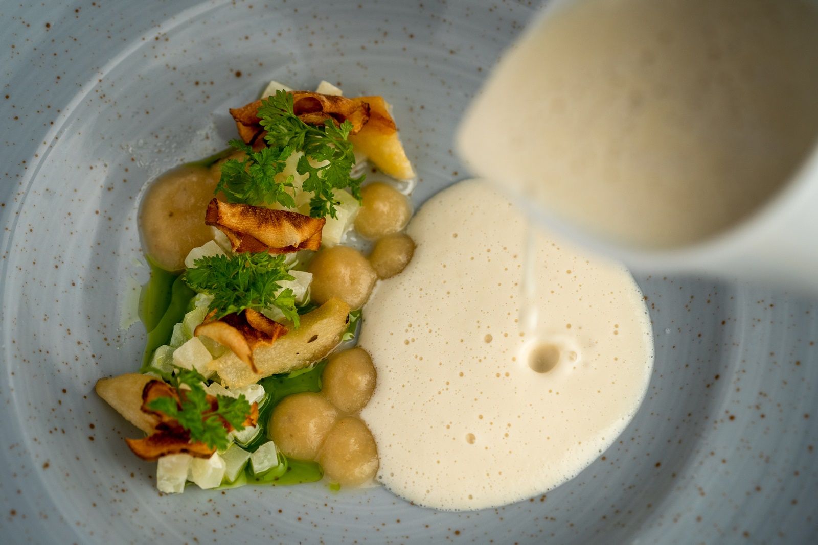 Gourmetgericht mit Schaum und Gemüse auf einem Teller.