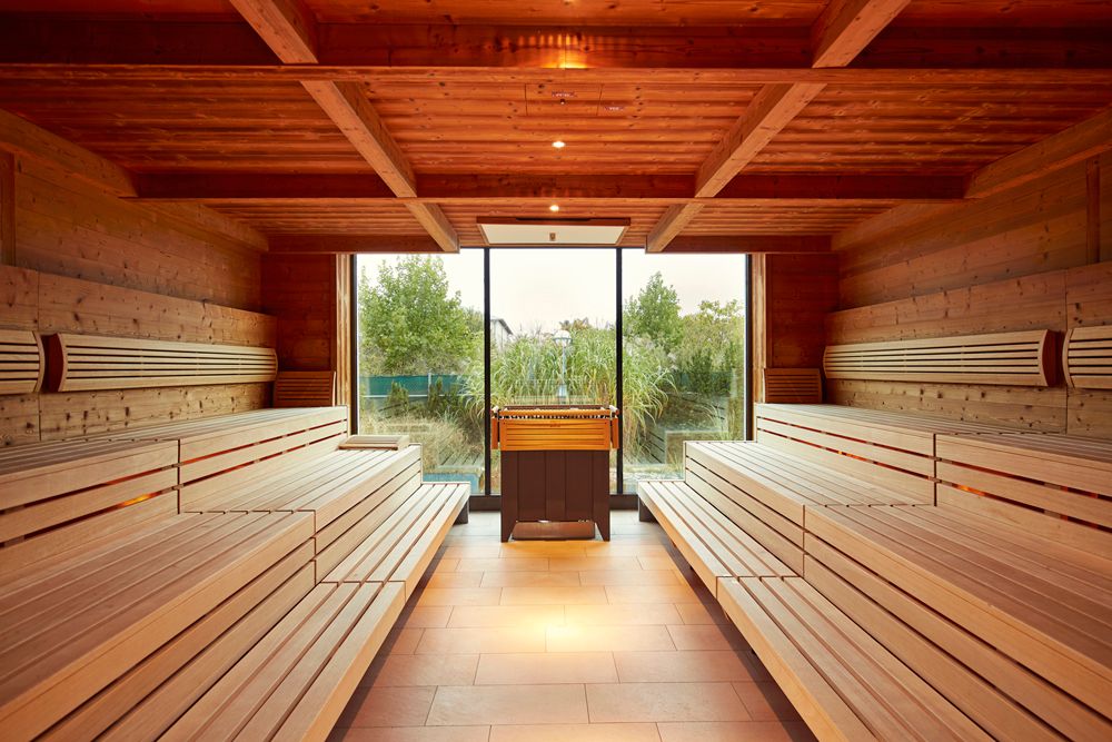Innenansicht einer Sauna mit Holzbänken und einem Fenster mit Blick ins Grüne.