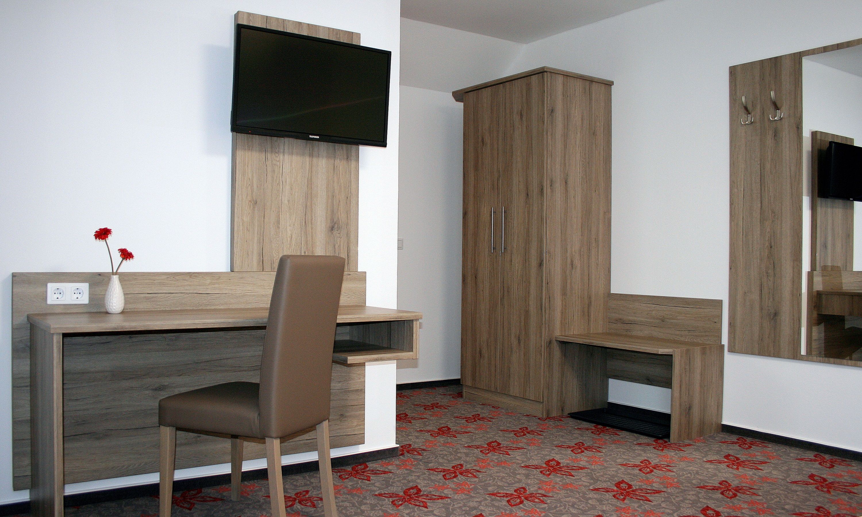 Hotelzimmer mit Schreibtisch, Stuhl, Fernseher und Schrank.