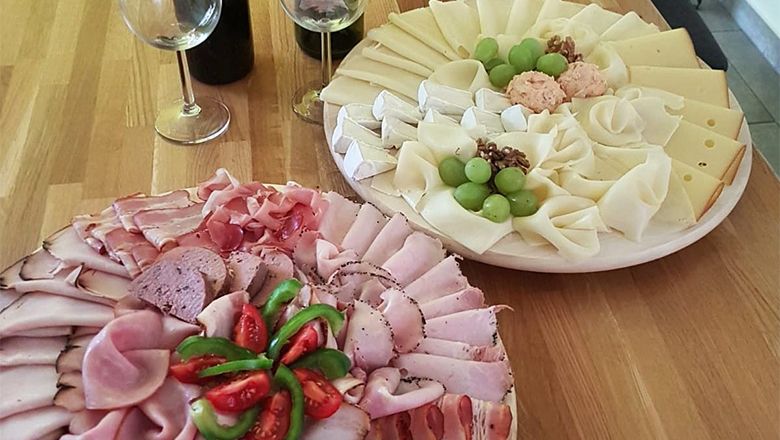 Zwei Platten mit Aufschnitt und Käse auf einem Holztisch, dekoriert mit Trauben und Tomaten.