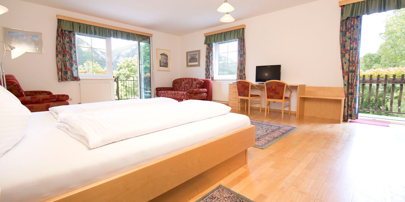 Doppelzimmer mit Holzboden und roter Couch sowie bunten Vorhängen