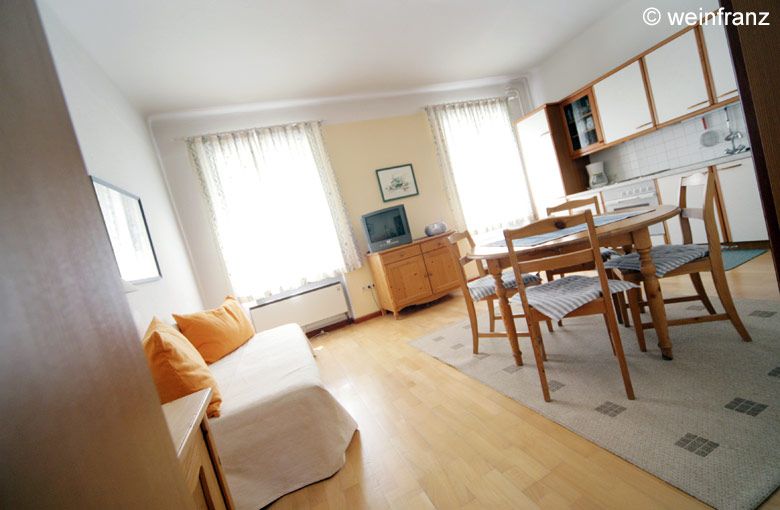 Helles Wohnzimmer mit Sofa, Esstisch und Küchenzeile.