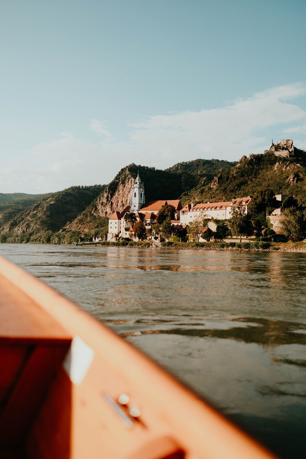 Die sanften Wellen der Donau spiegeln das warme Licht des Sonnenuntergangs wider, während die malerische Landschaft der Wachau in goldene Töne getaucht wird. Historische Gebäude und üppige Weinberge säumen das Ufer und laden zu einer entspannenden Bootstour ein, die die Seele berührt.