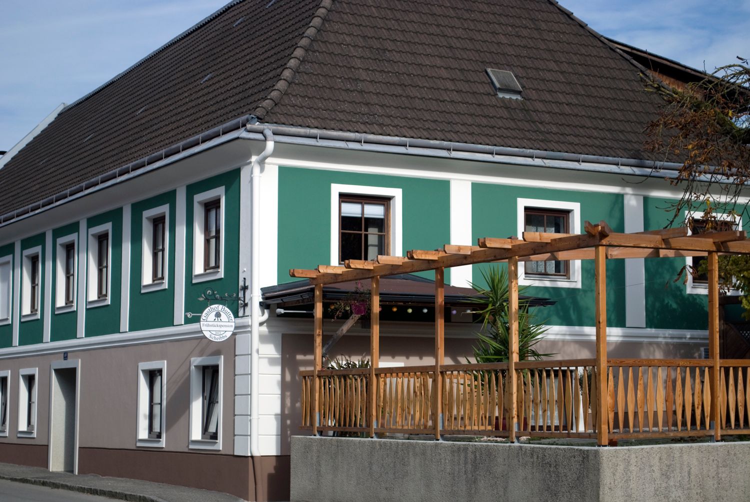 Außenansicht einer Frühstückspension mit grün-weißer Fassade und Holzpergola.