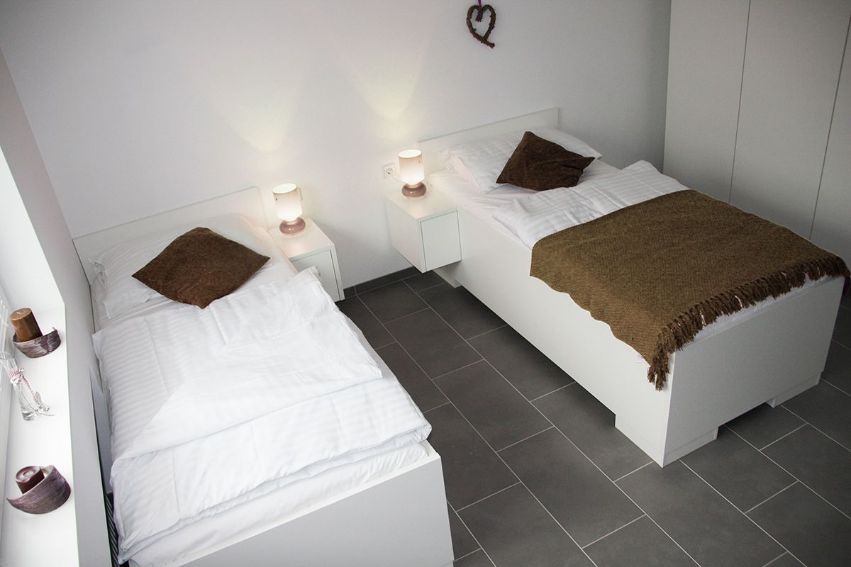 Zwei Einzelbetten in einem modernen, hellen Zimmer mit weißen Möbeln und braunen Decken.
