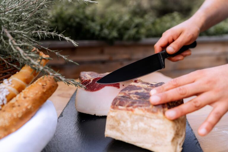 Person schneidet Speck auf einem Holzbrett.