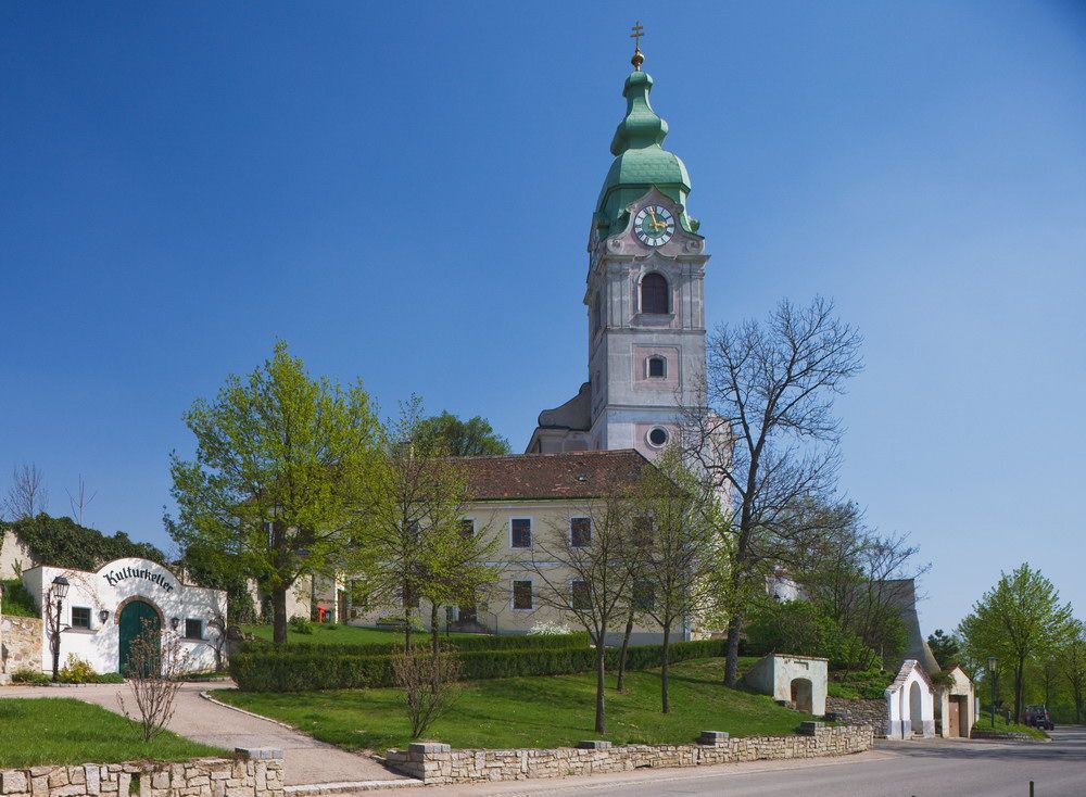 Kirche in Unterretzbach mit grünem Turm und umliegenden Gebäuden.