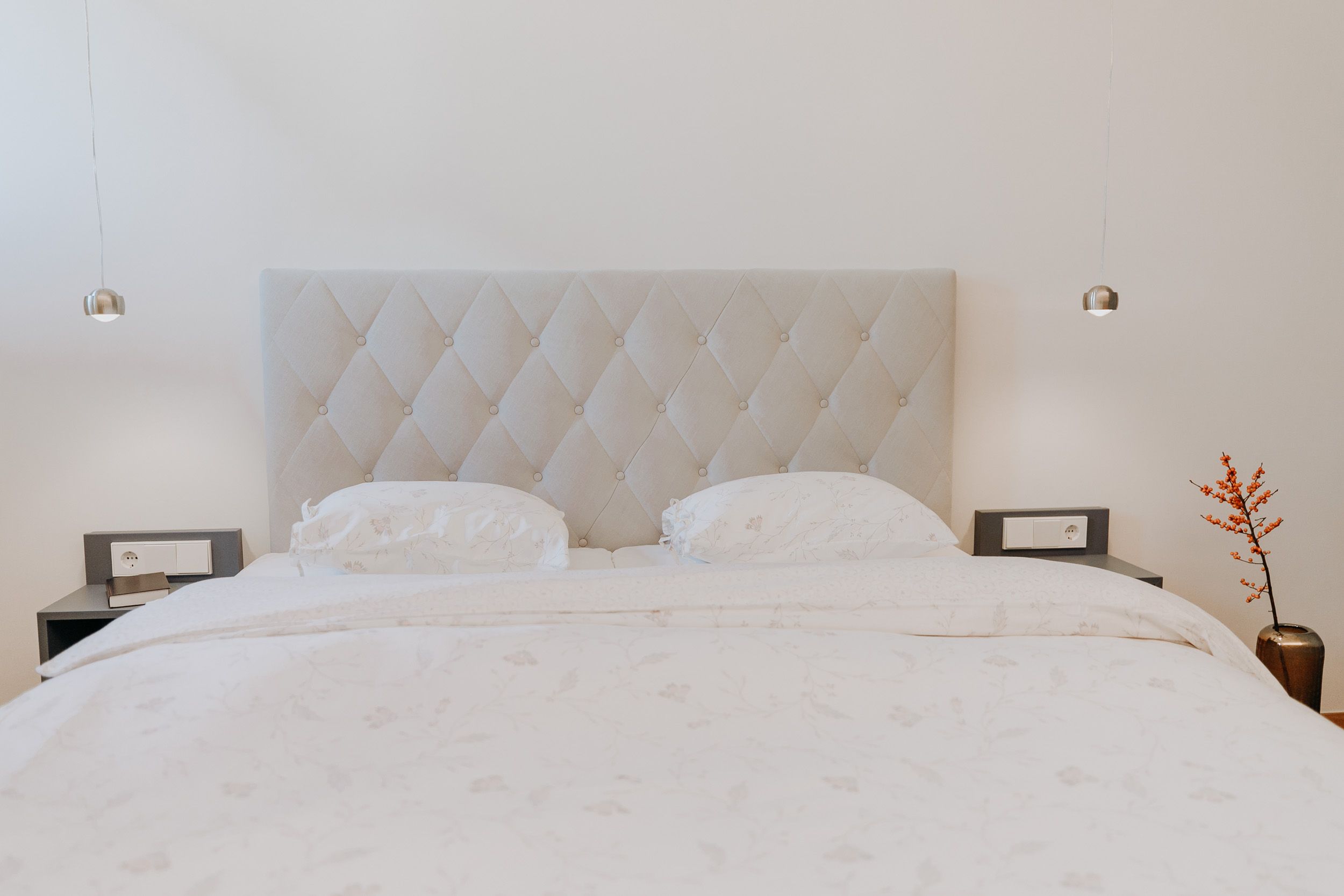 Ein elegantes Schlafzimmer mit einem großen Bett, zwei Nachttischen und einer Vase mit roten Beeren.