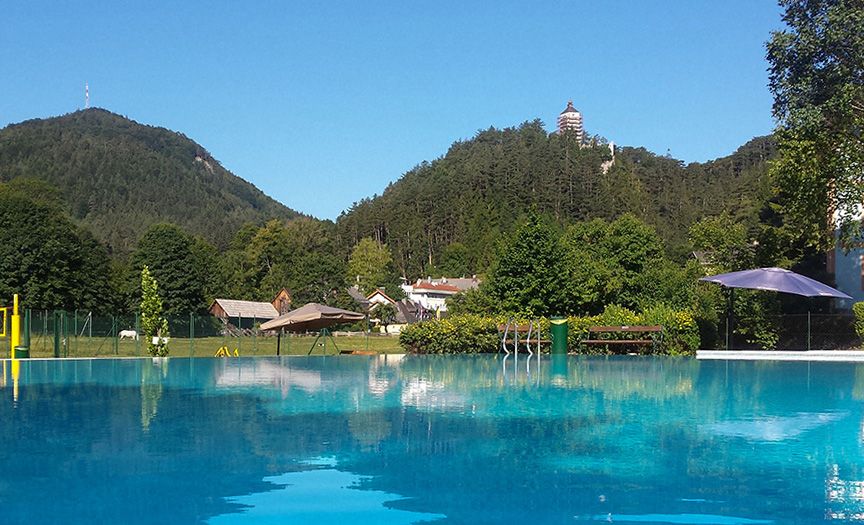 Freibad mit Blick auf bewaldete Hügel und einen Turm in der Ferne.