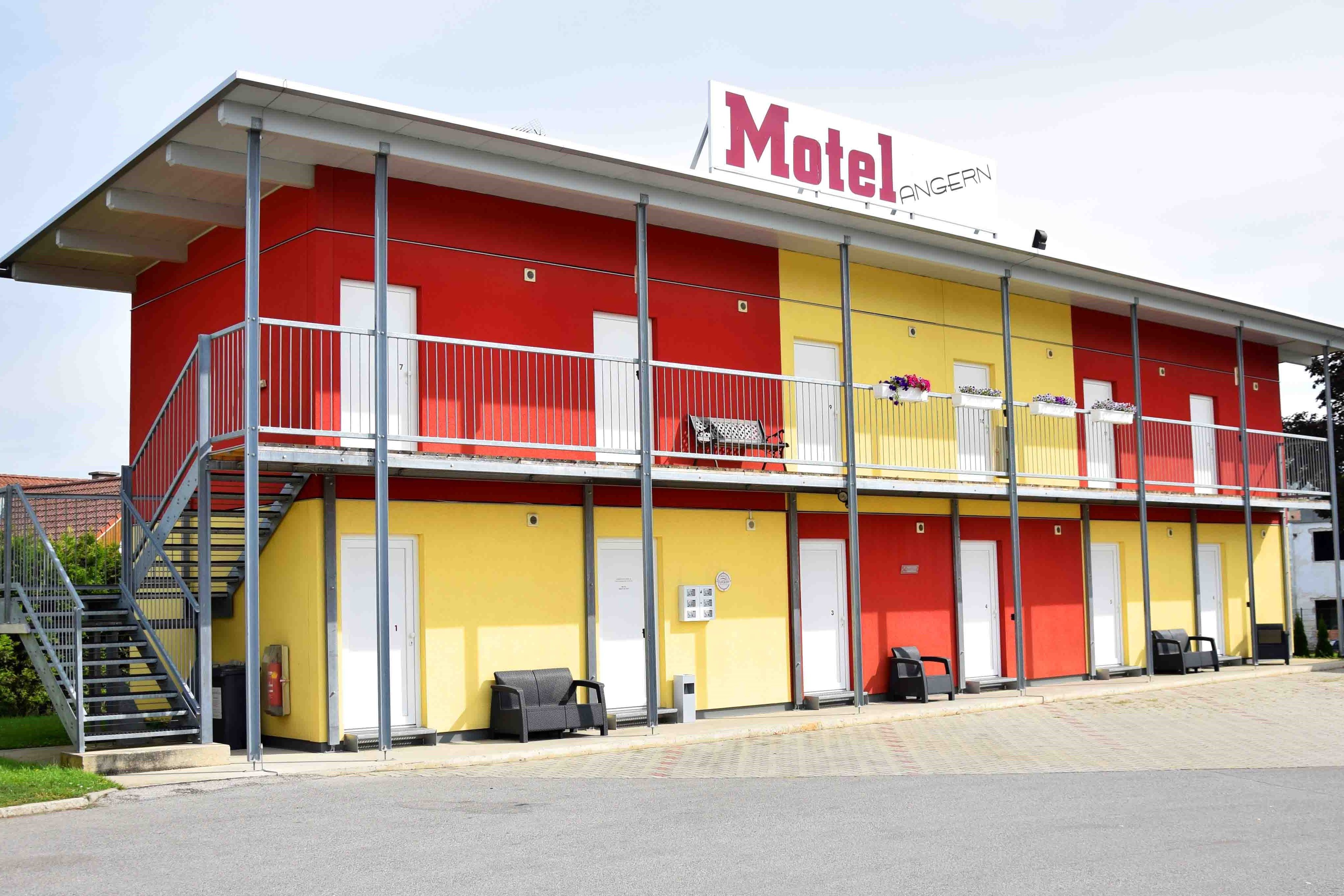 Zweistöckiges Motelgebäude mit gelben und roten Wänden, Treppe und Balkon.